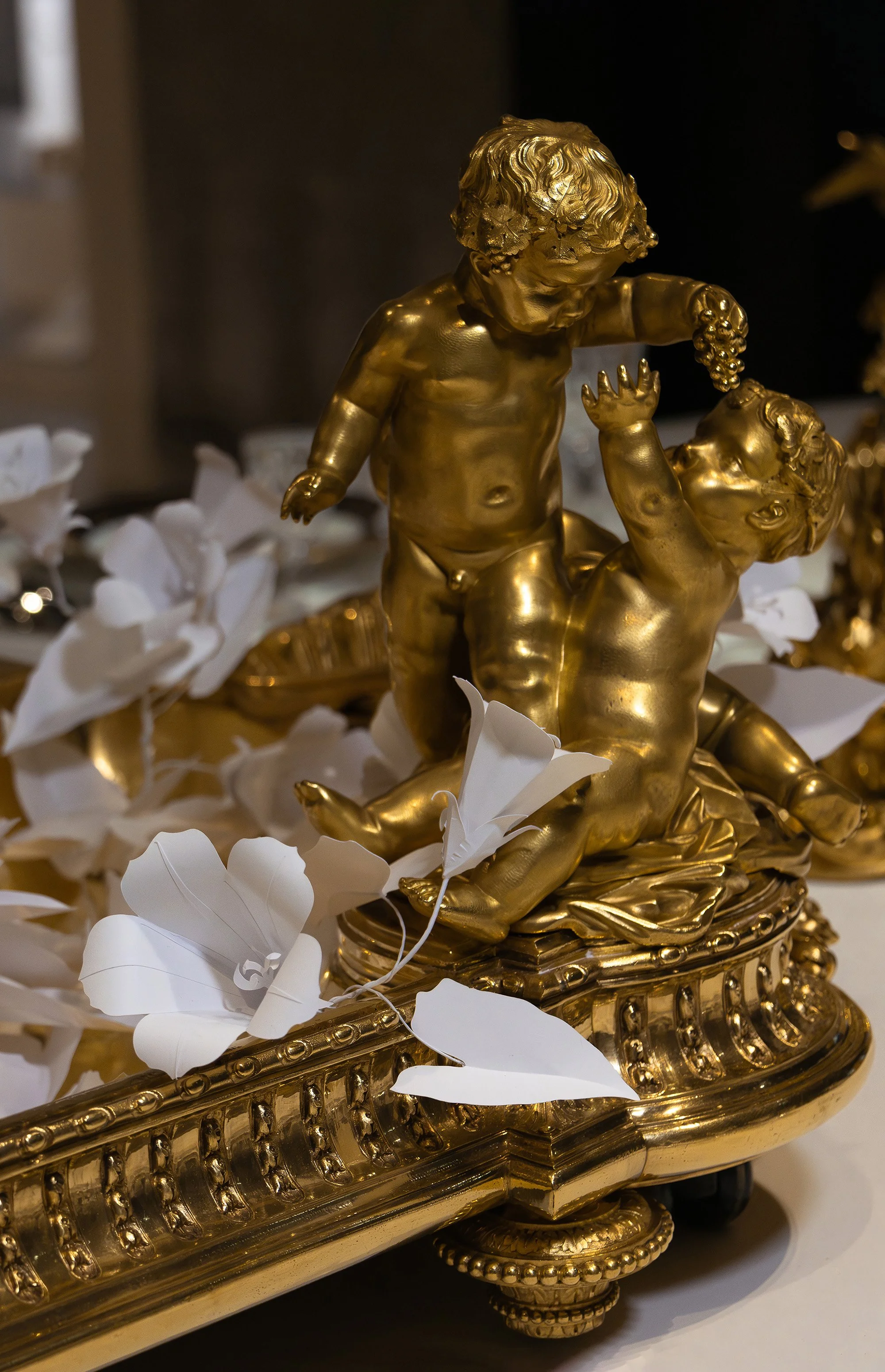 White paper bindweed flowers weaving around gilded cherubs on the central Christofle jardinière, exhibition scenography at the Musée des Arts Décoratifs, Paris.