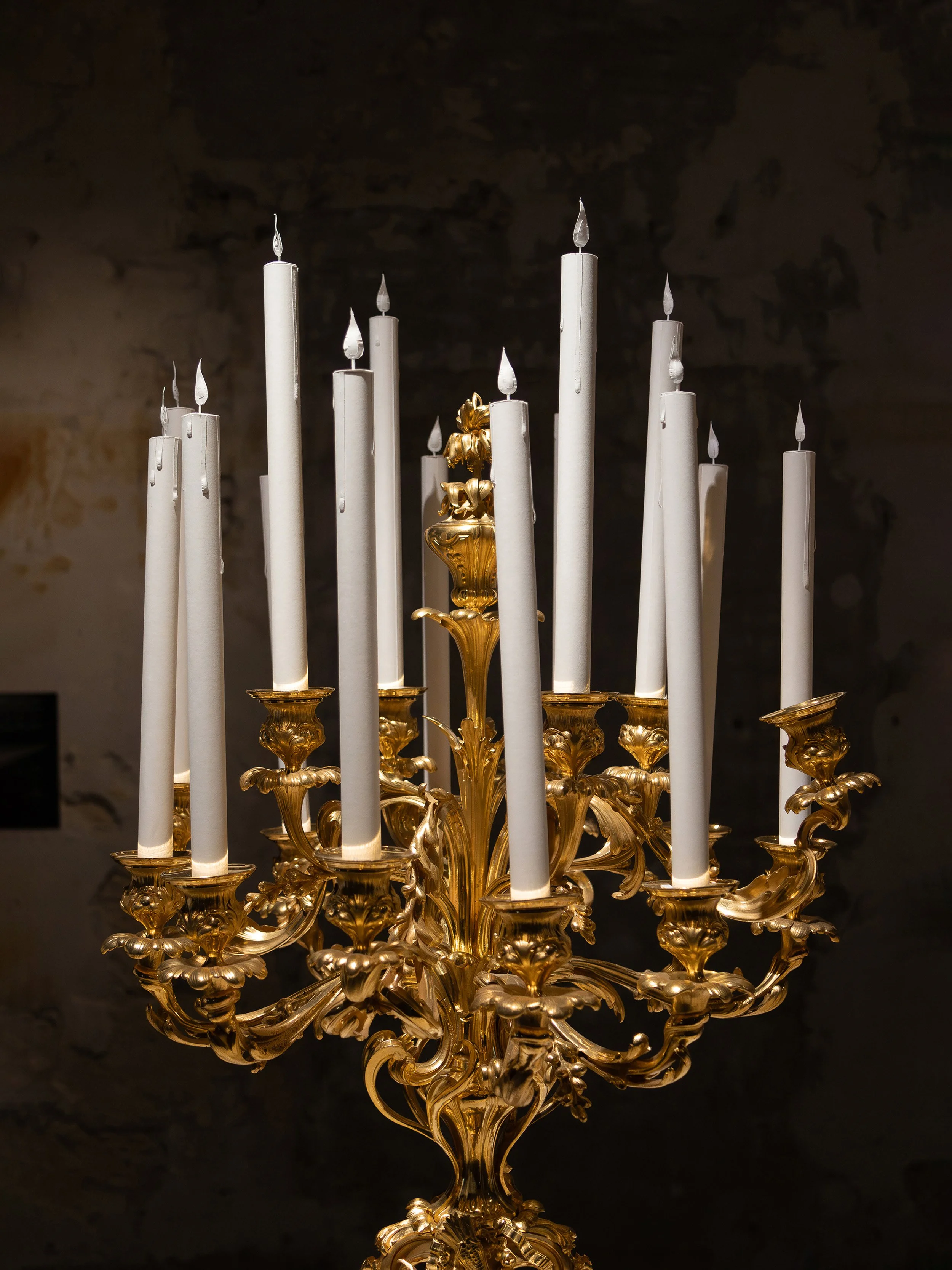 Gilded Christofle candelabra adorned with white paper candles featuring sculpted dripping wax and delicate paper flames, created for “Christofle, a brilliant story” exhibition at the Musée des Arts Décoratifs, Paris.
