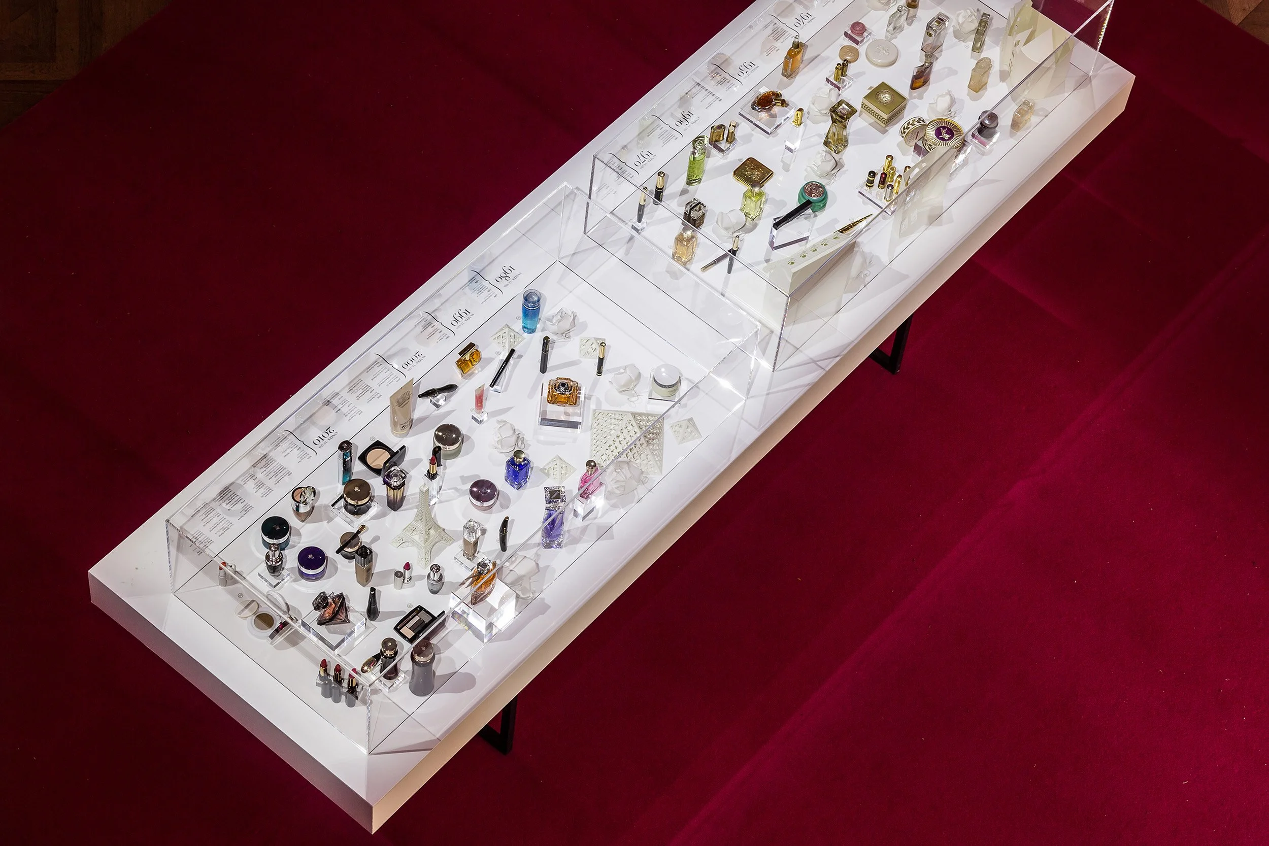 Overhead view of the illuminated display table presenting Lancôme archival products and white paper architectural models