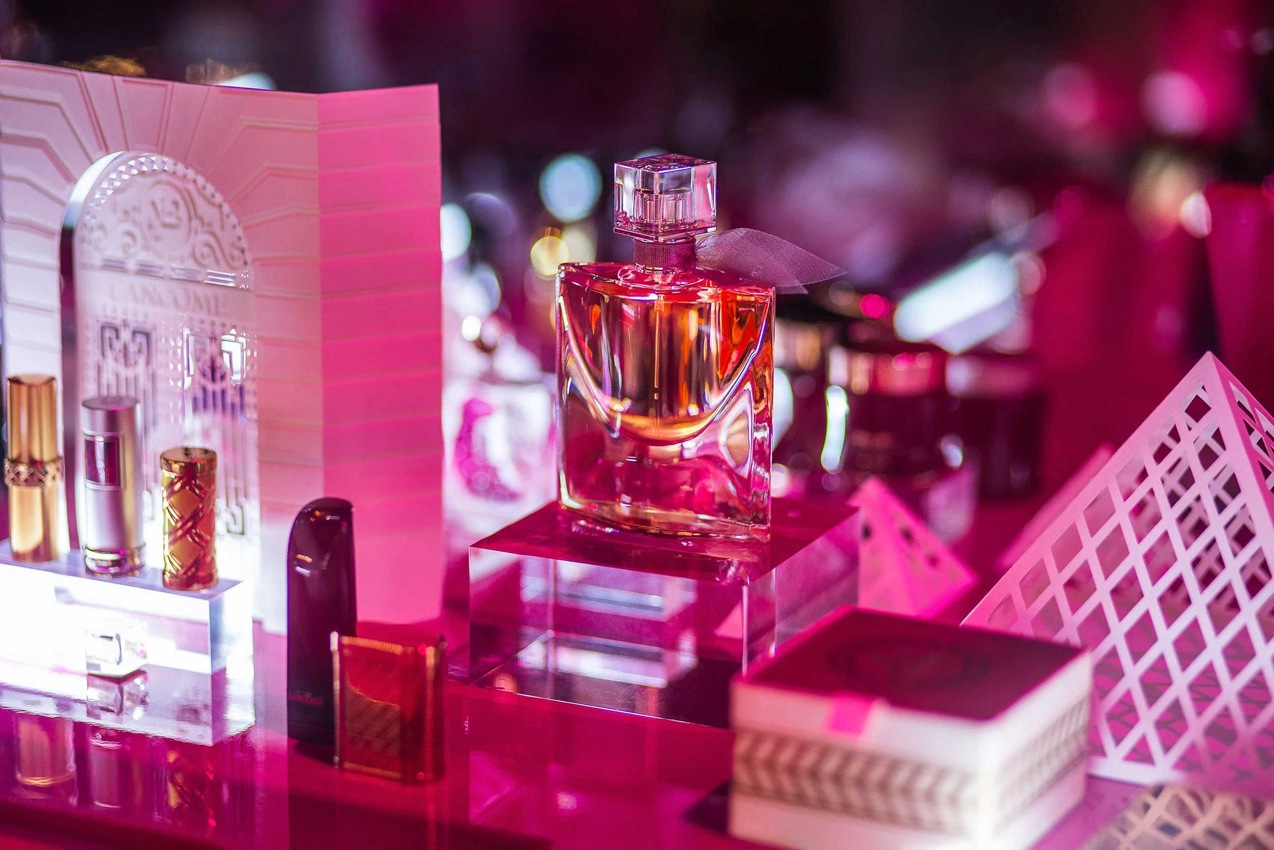 Iconic La Vie Est Belle perfume bottle surrounded by white paper models of the Institut Lancôme façade and the Louvre Pyramid within the anniversary scenography