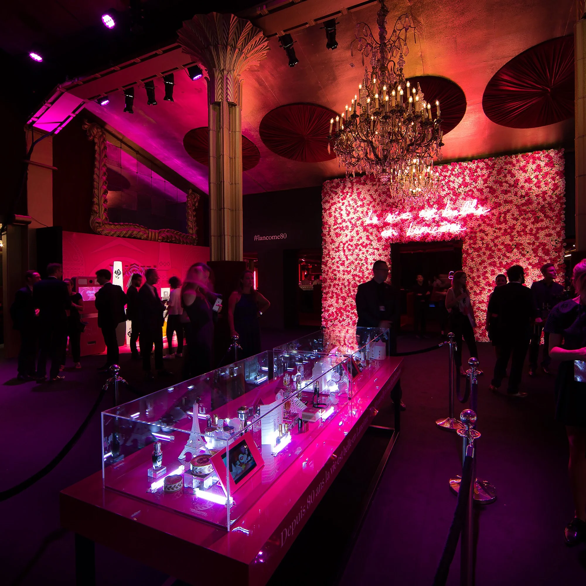 Event scenography in the entrance hall of Casino de Paris, featuring an illuminated central display table and a large rose-covered backdrop for Lancôme’s 80th anniversary