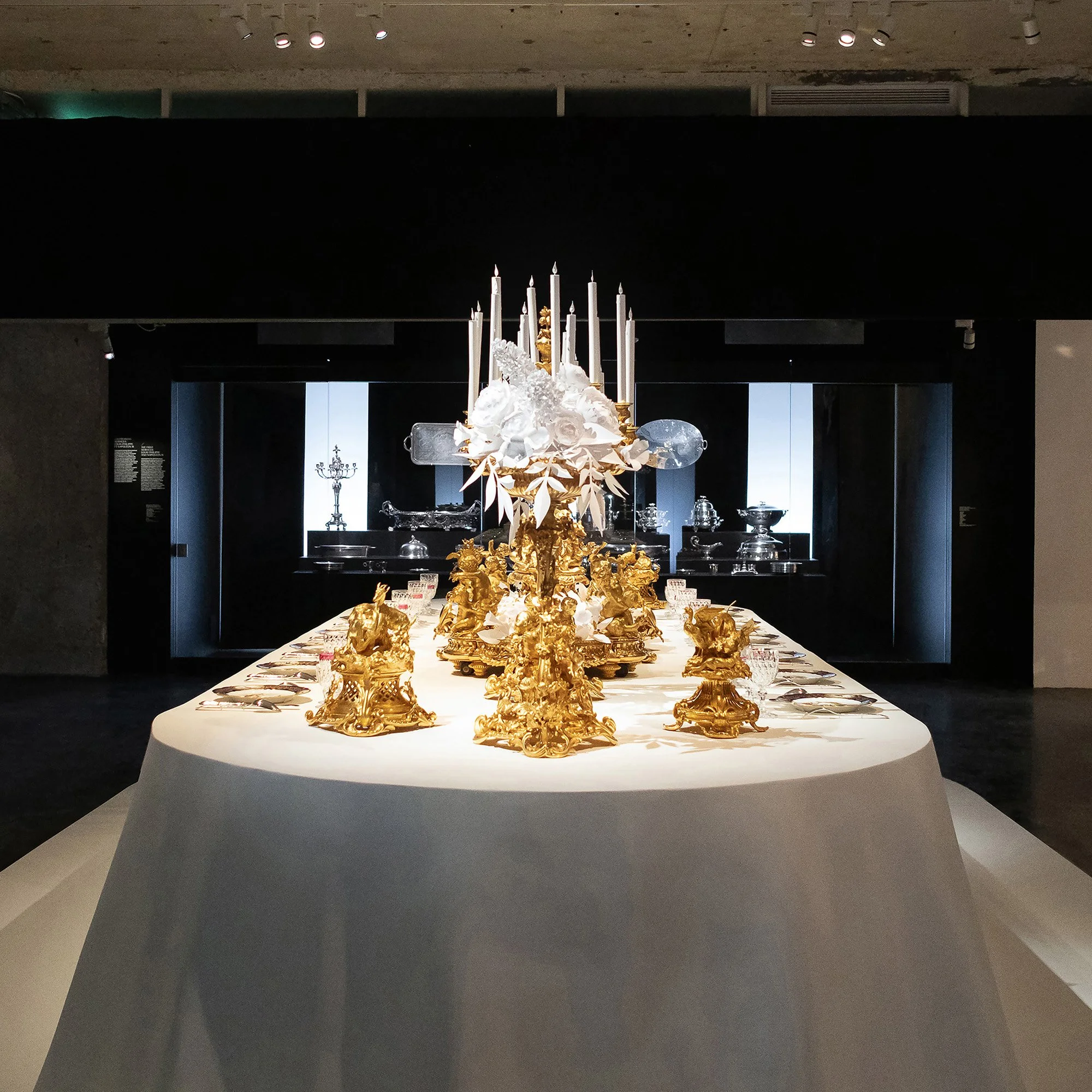 Banquet table scenography with gilded Christofle centerpieces and white paper floral installation at the Musée des Arts Décoratifs, Paris.