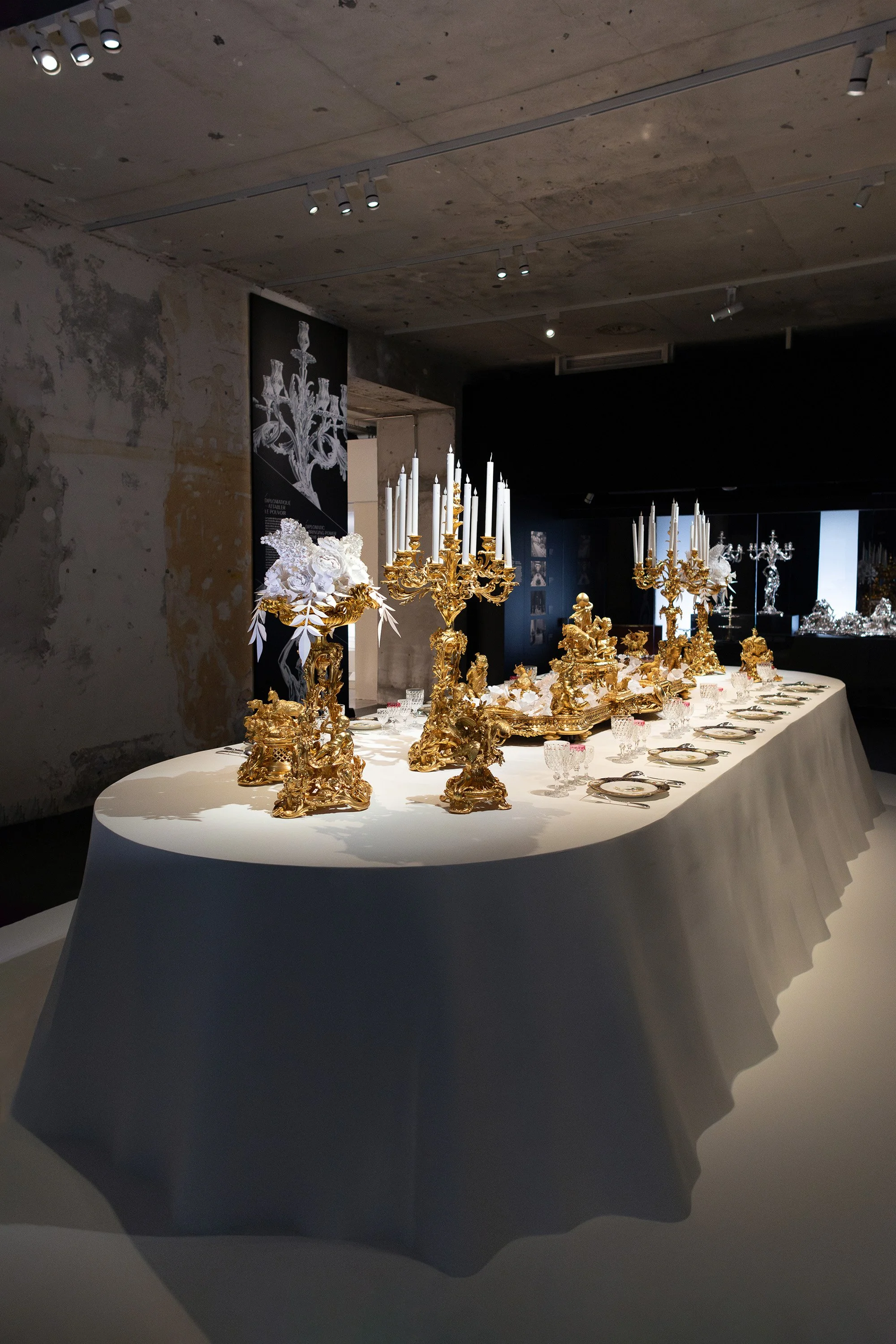 Side view of banquet table featuring gilded Christofle pieces and white paper floral compositions at the Musée des Arts Décoratifs, Paris.