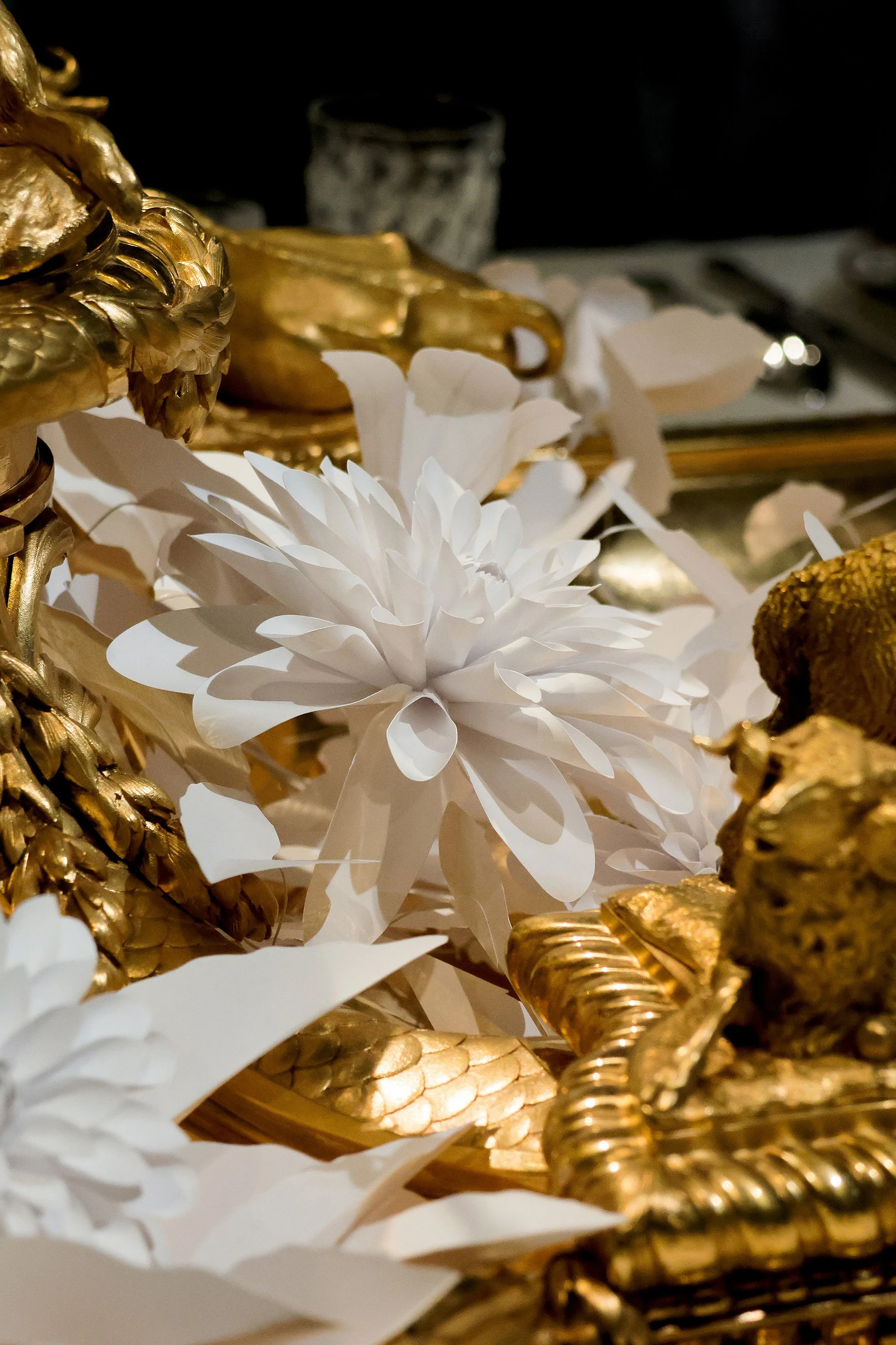 Close-up of a white paper dahlia in bloom within the gilded Christofle centerpiece, exhibition scenography at the Musée des Arts Décoratifs, Paris.