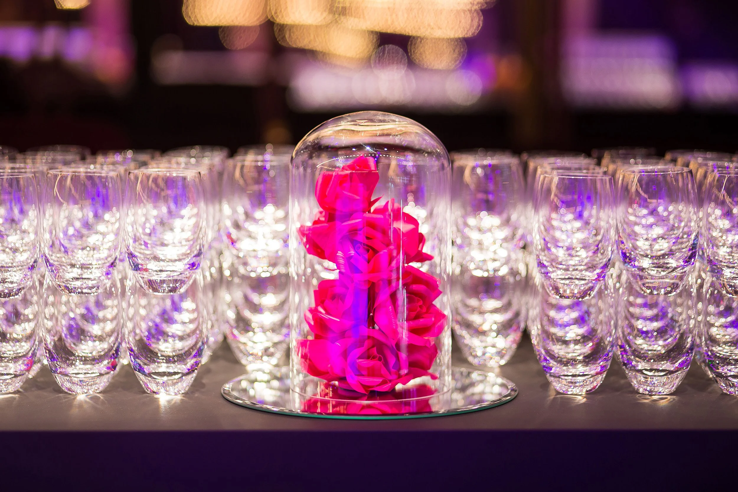 Accumulation of bright pink paper roses under a glass cloche at the Casino de Paris, surrounded by rows of glassware on the bar