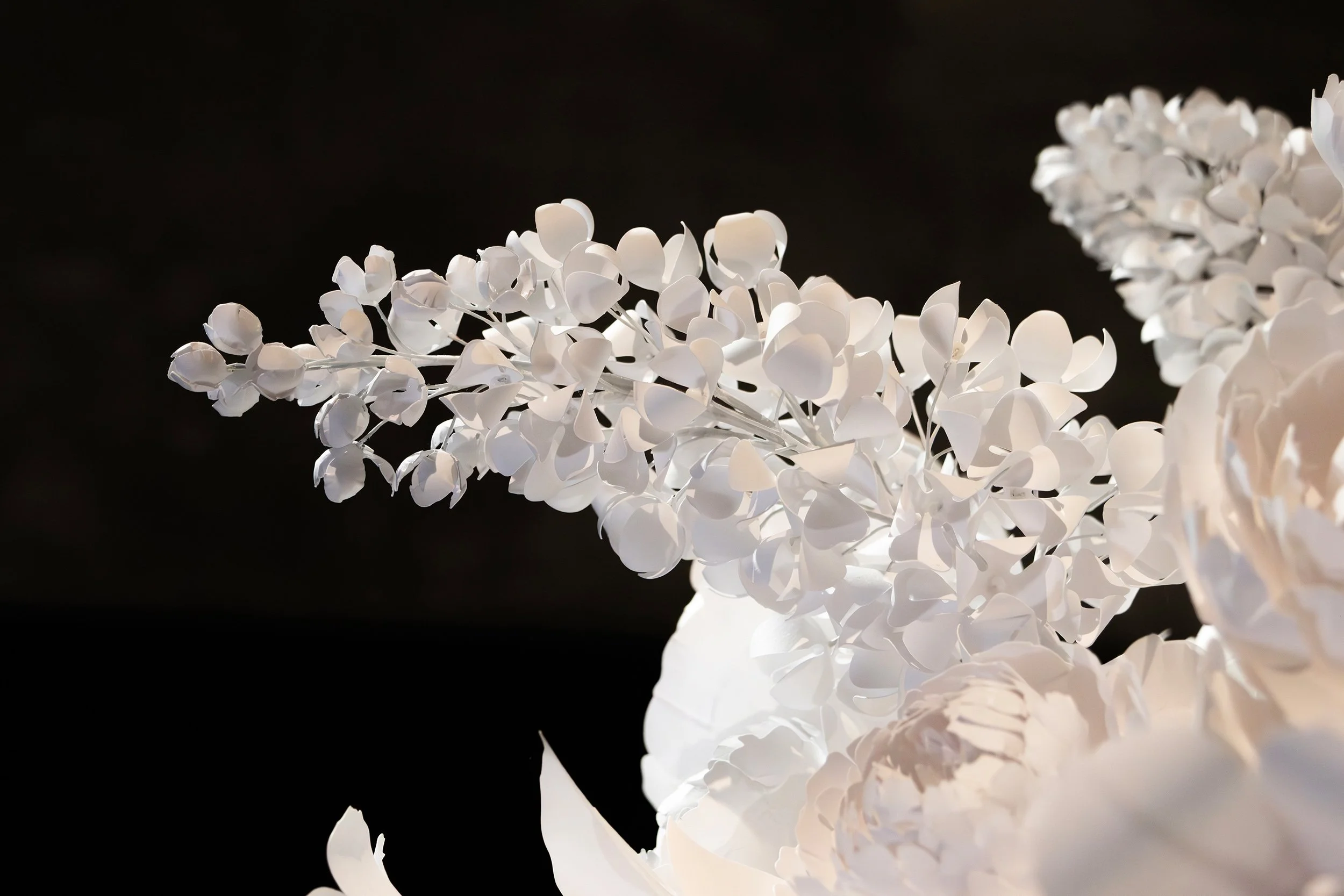 Close-up of suspended white paper lilac branch, delicately arranged within Christofle exhibition scenography, Musée des Arts Décoratifs, Paris.