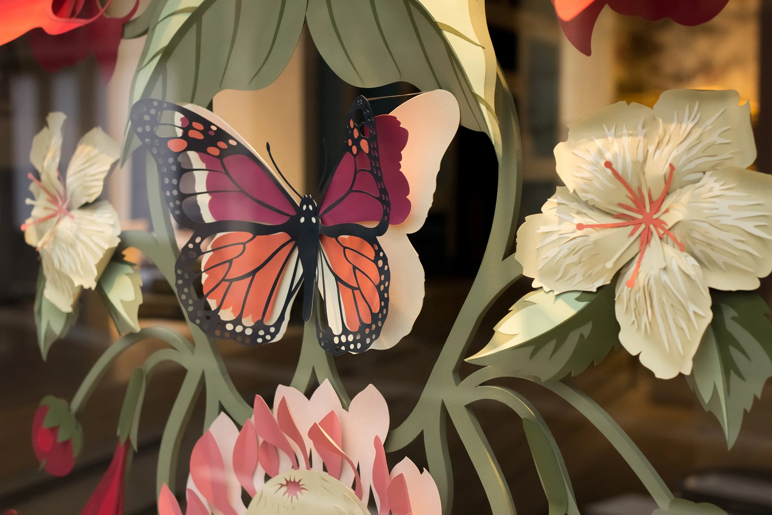 Detail of layered paper flowers and butterfly from a window display inspired by the Asterid wallpaper pattern