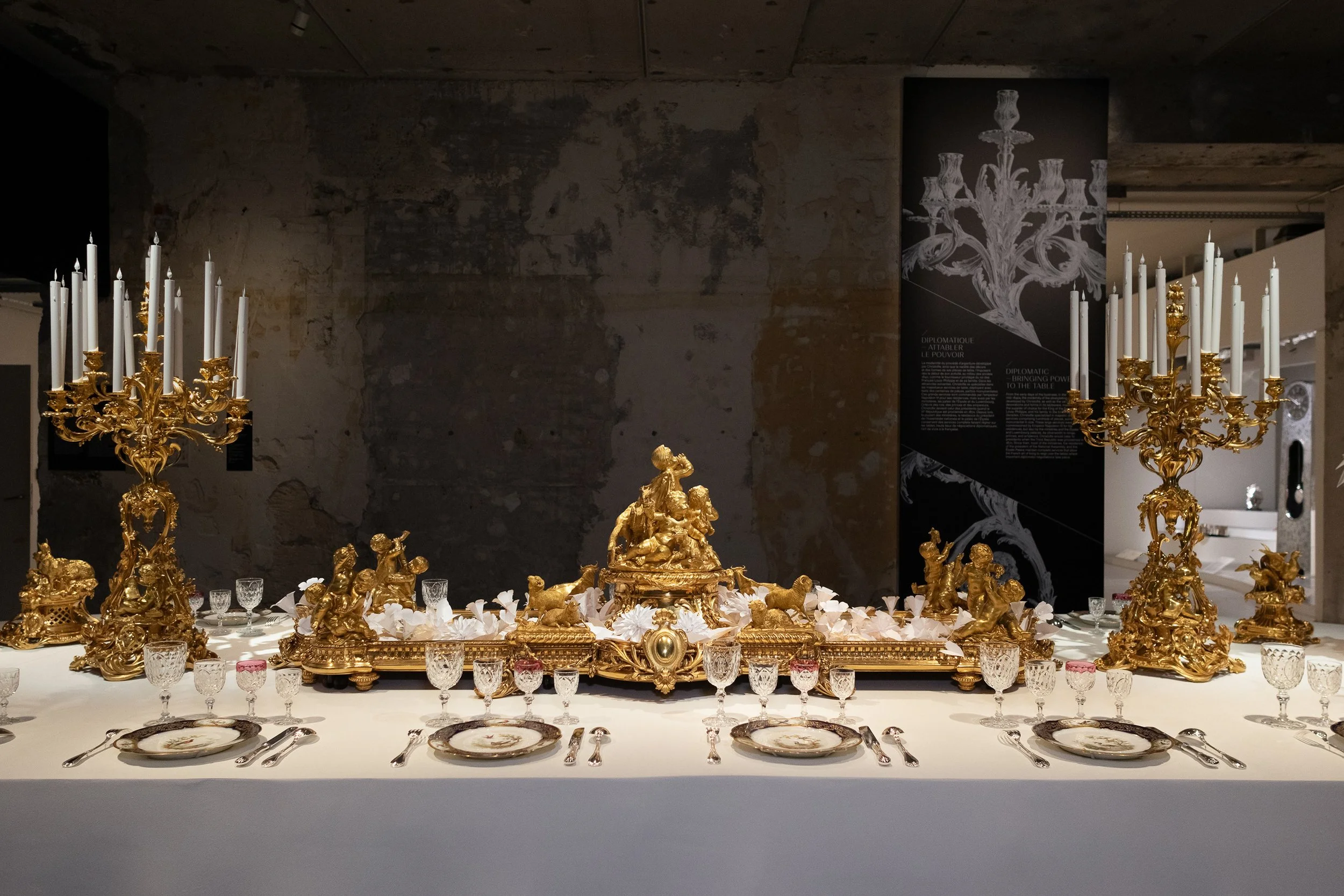 Monumental banquet table installation featuring gilded Christofle candelabras and white paper floral arrangement at the Musée des Arts Décoratifs, Paris.