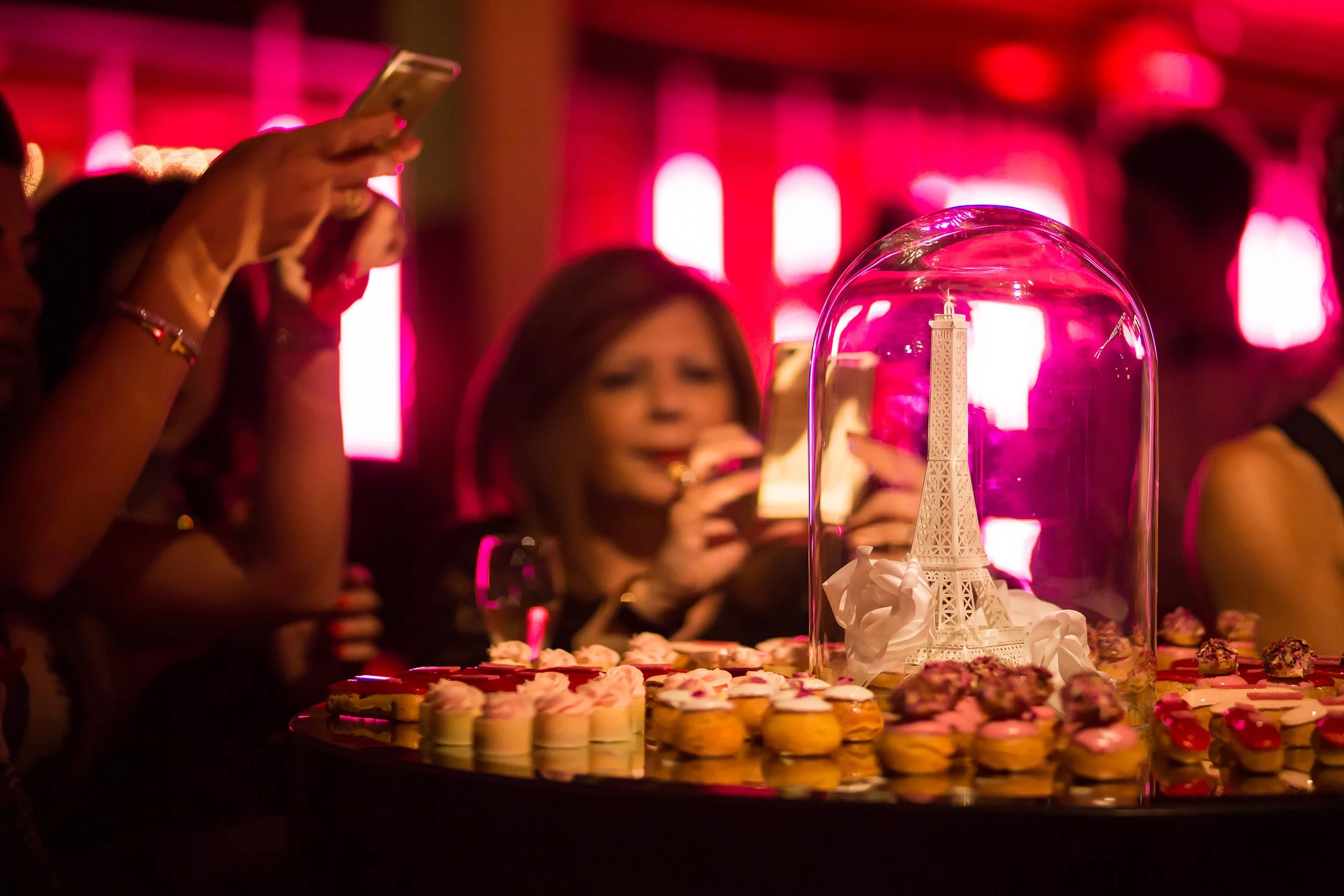 Paper Eiffel Tower displayed under a glass cloche, surrounded by pink pastries during the Lancôme anniversary event at Casino de Paris