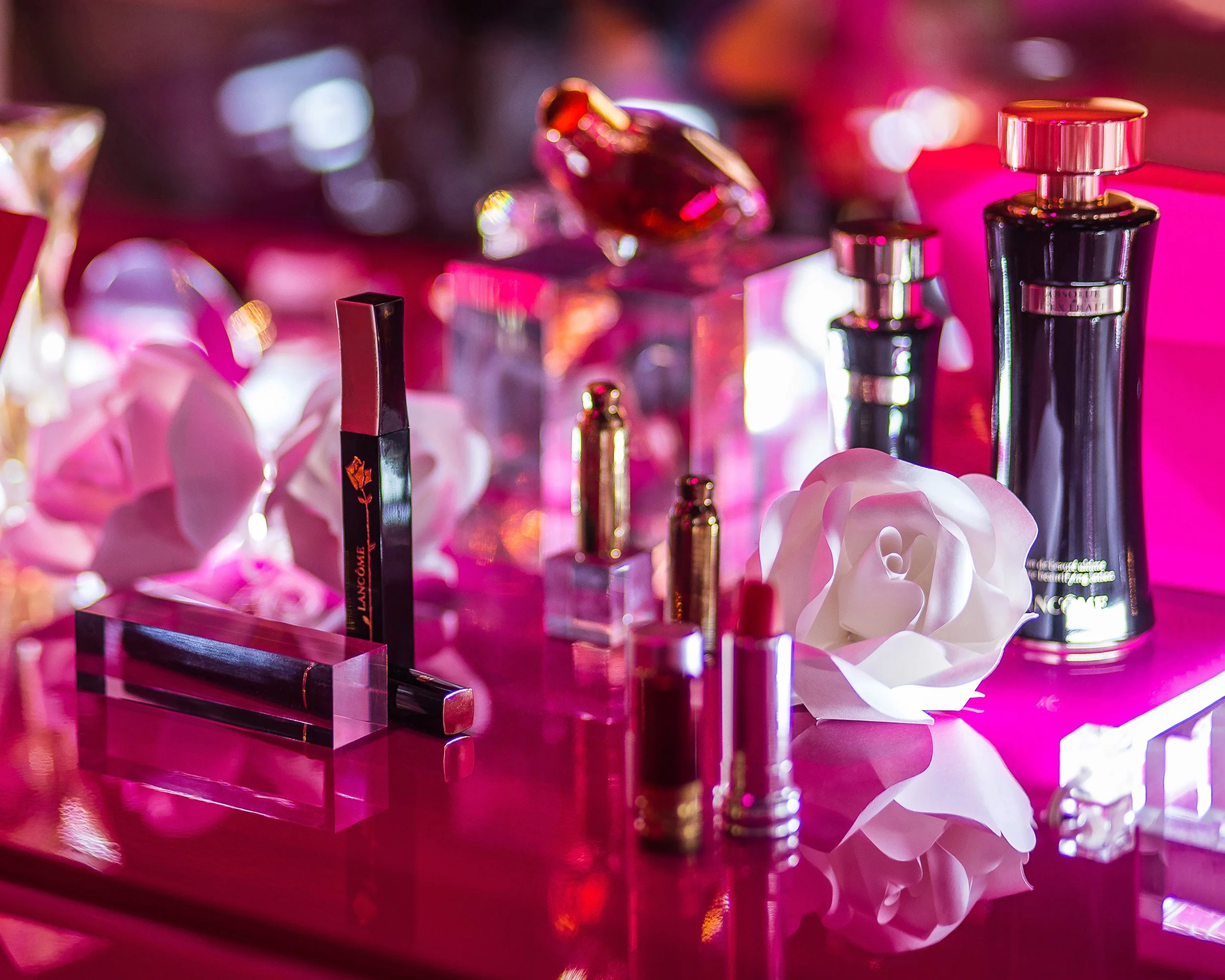 Lancôme fragrance and makeup display with white paper rose on glossy pink table, event set design