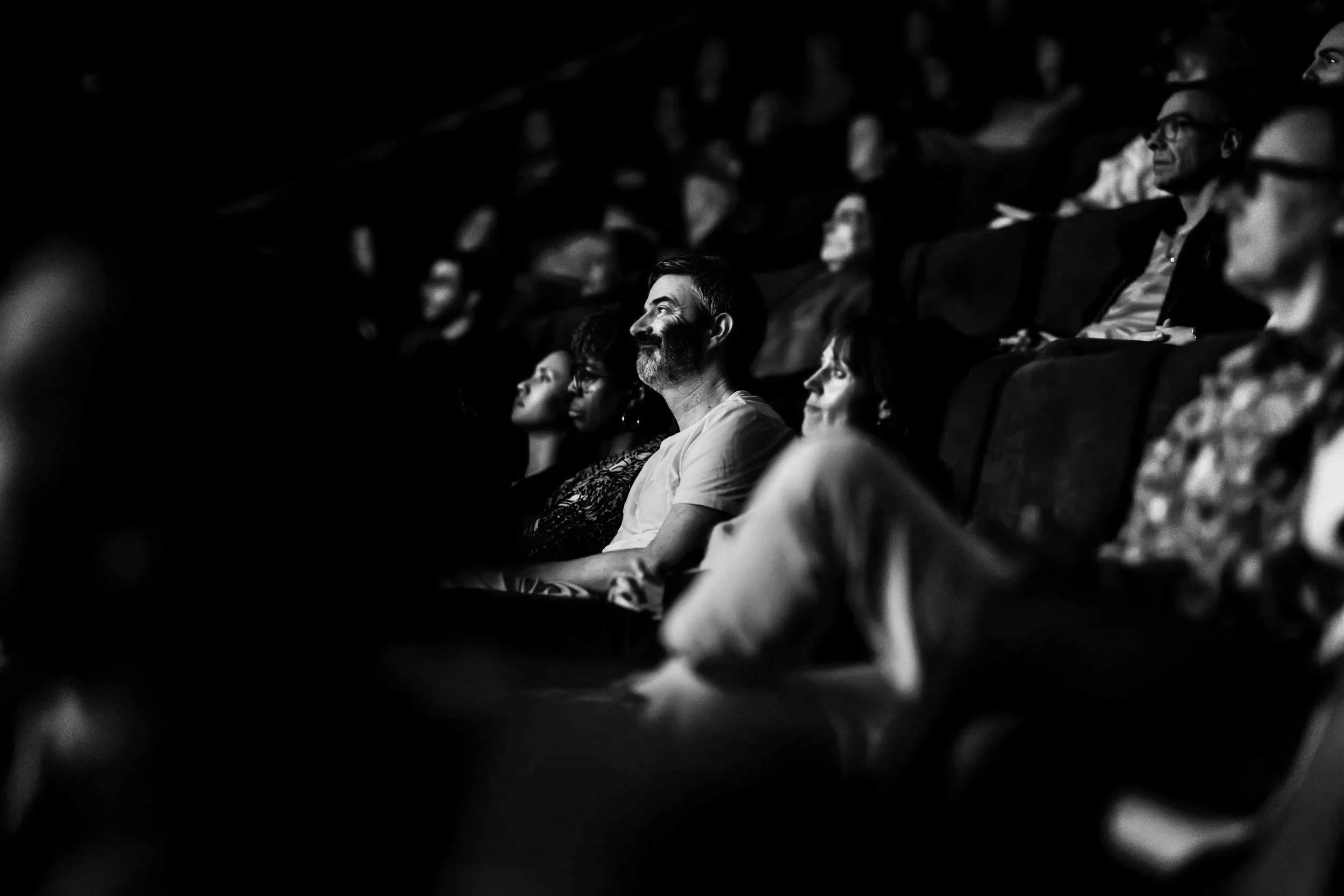 Audience sitting in a dark theater watching a performance or film with focused expressions.