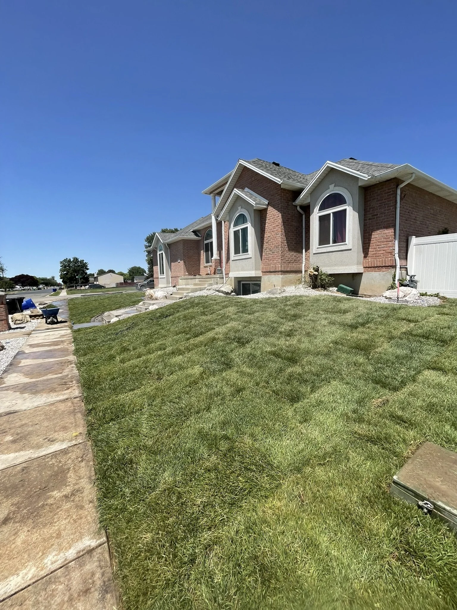 A brick house with arched windows, a gray roof, and a lush green lawn under a clear blue sky.