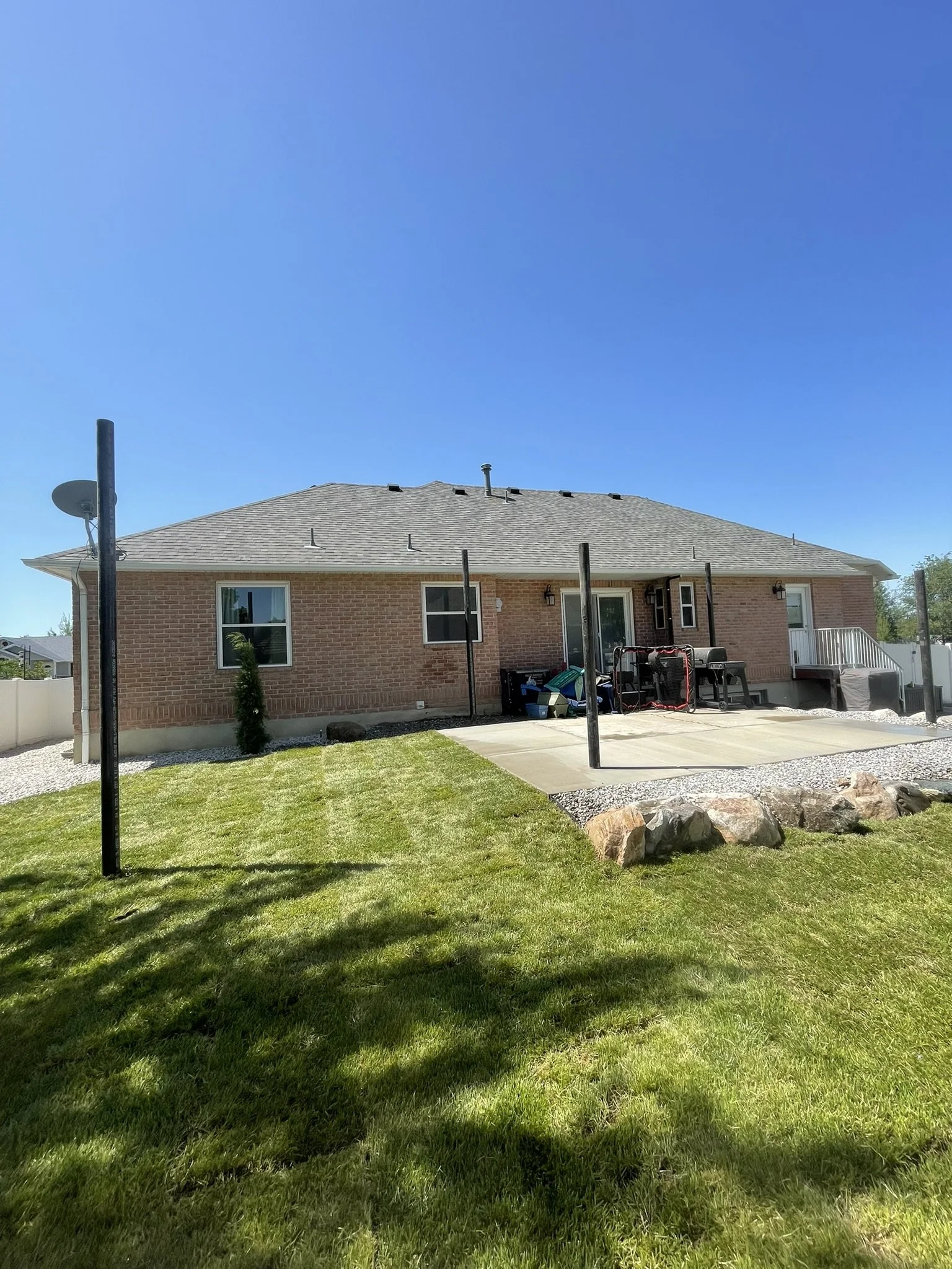 Backyard of a brick house with a small lawn, concrete patio, and a clothesline pole, under a clear blue sky.