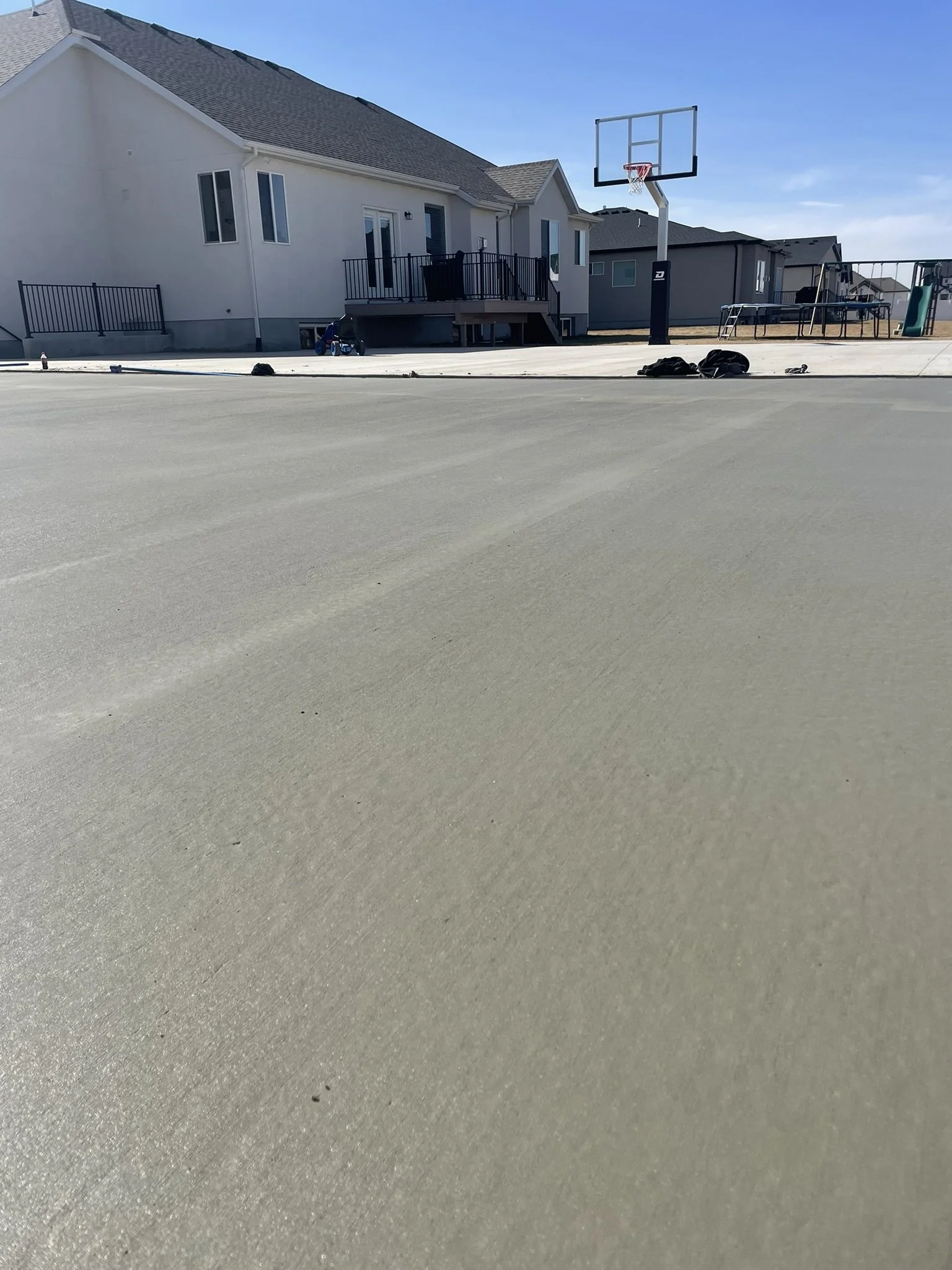 View of a backyard with a basketball hoop, house with a deck, and playground in the background, taken from a low angle close to the ground.