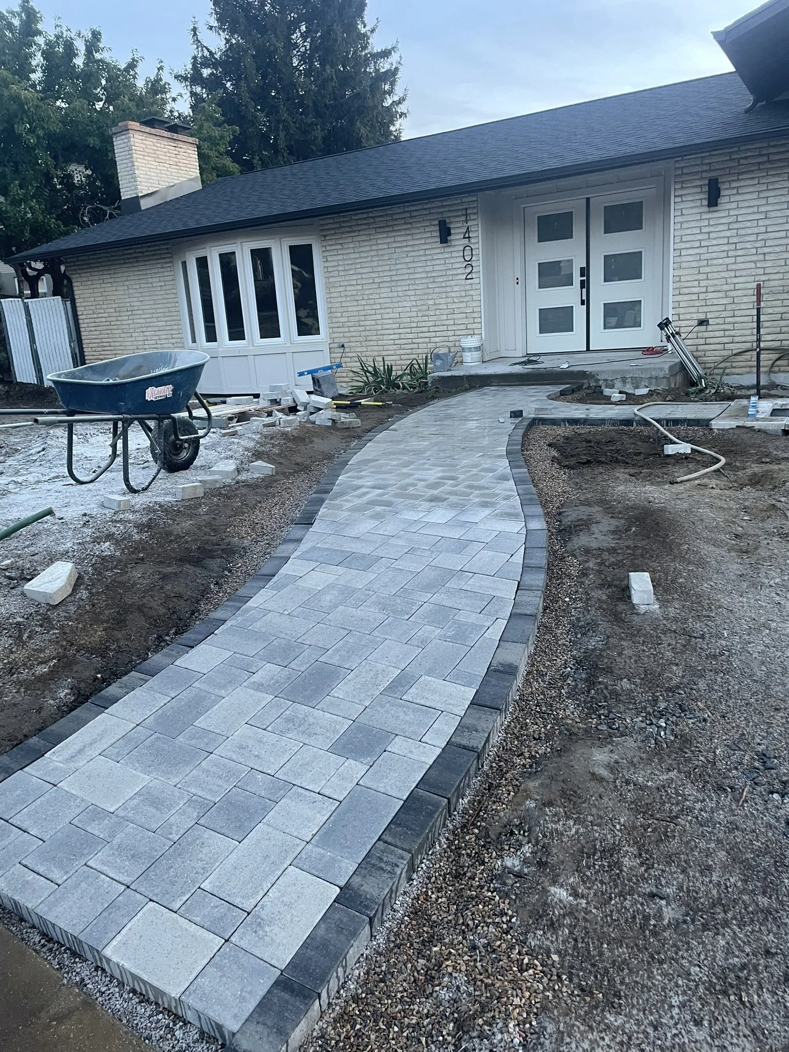 A newly paved stone walkway leading to the front door of a house under construction, with construction tools and materials nearby.