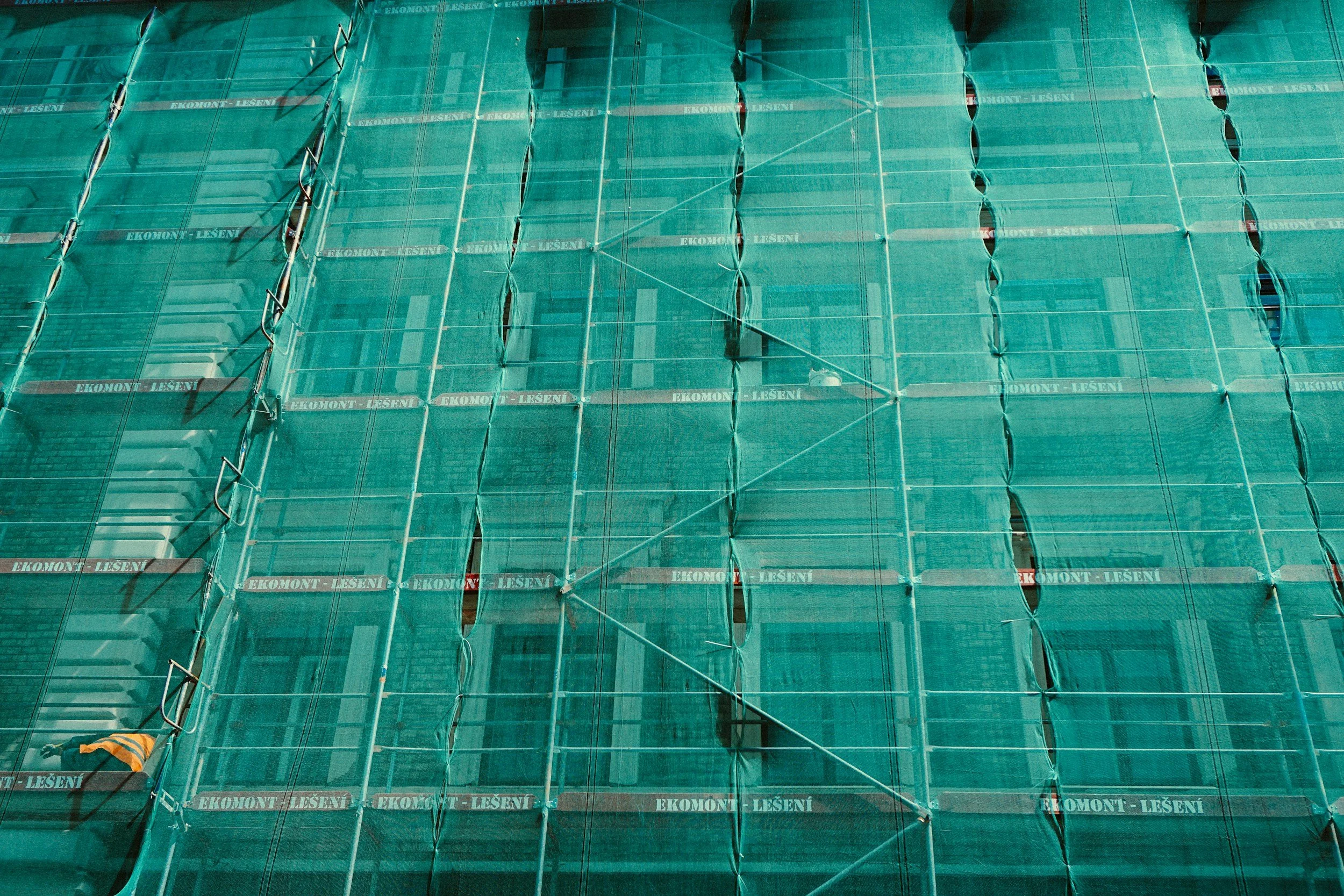tall building under construction with green net over side