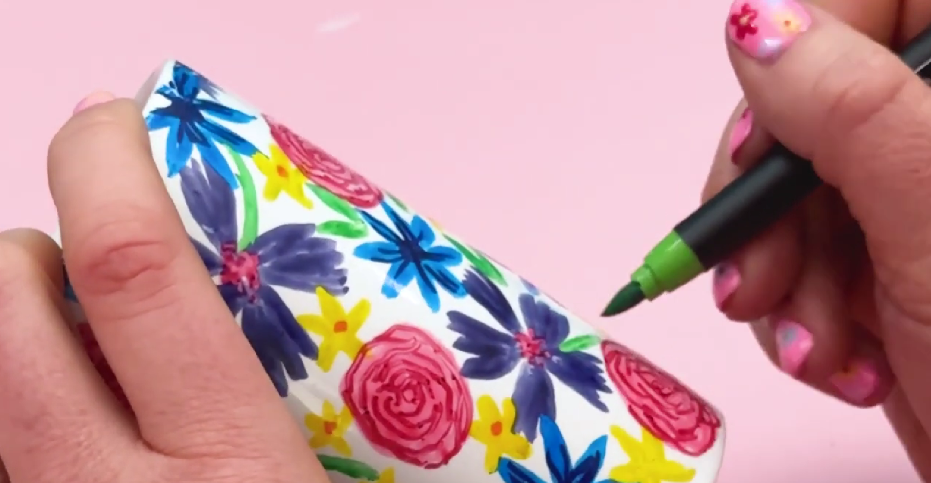 Painting green leaves and stems around floral design on ceramic pen pot using brush pen