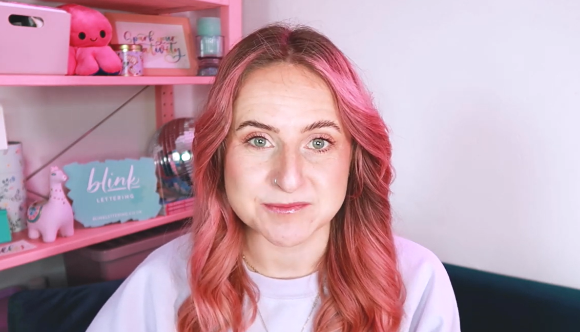 Milly, calligraphy tutor and founder of Blink Lettering, smiling at camera in front of a calligraphy workspace