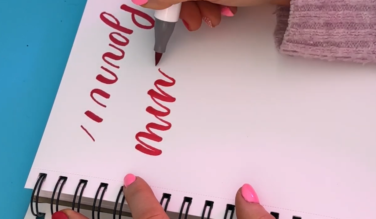 The word "minimum" written in bouncy modern calligraphy using an Ohuhu Cherry Pink brush marker, showing the flat opaque ink finish