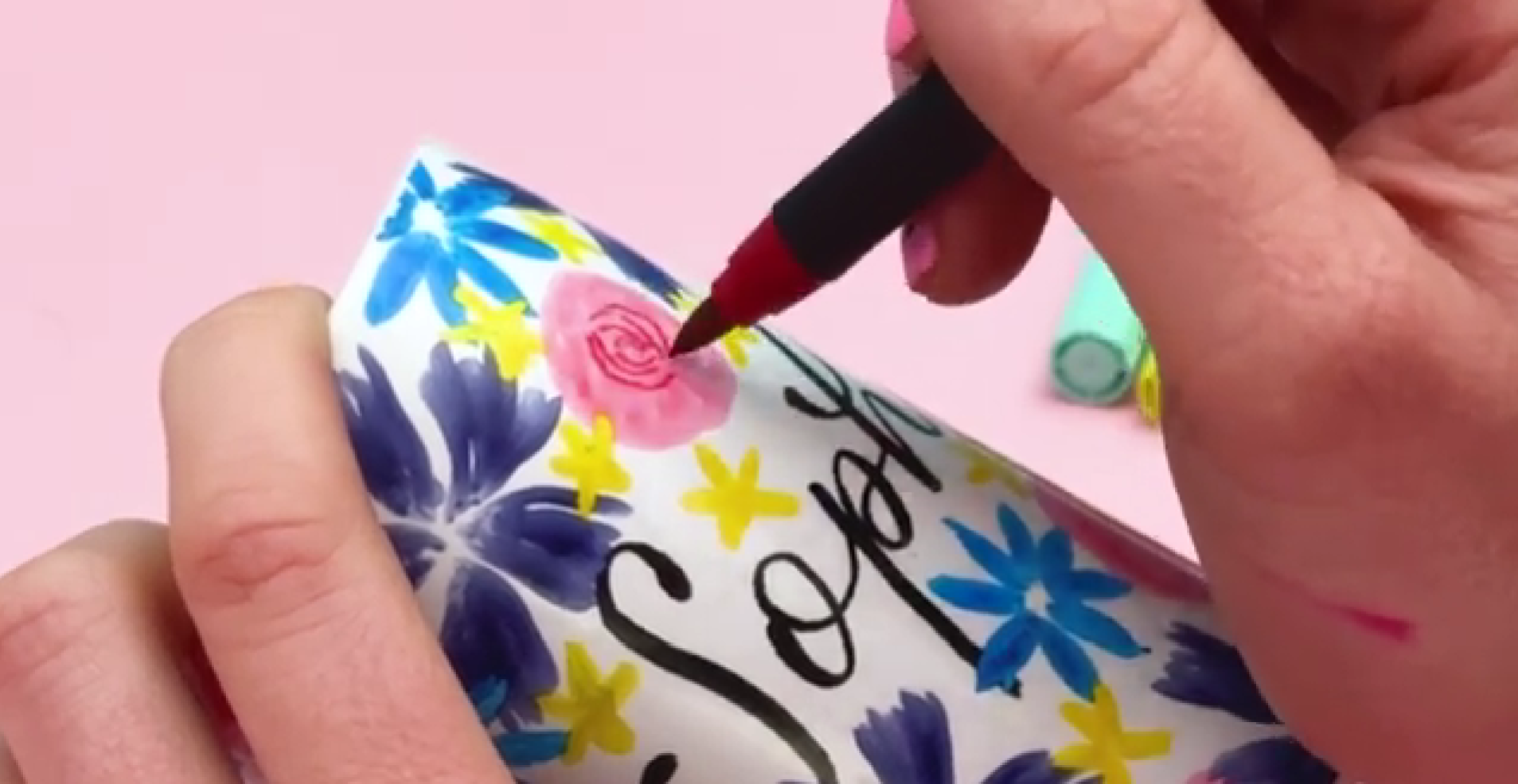 Drawing spiral lines inside pink roses to create petal detail and depth on ceramic pen pot