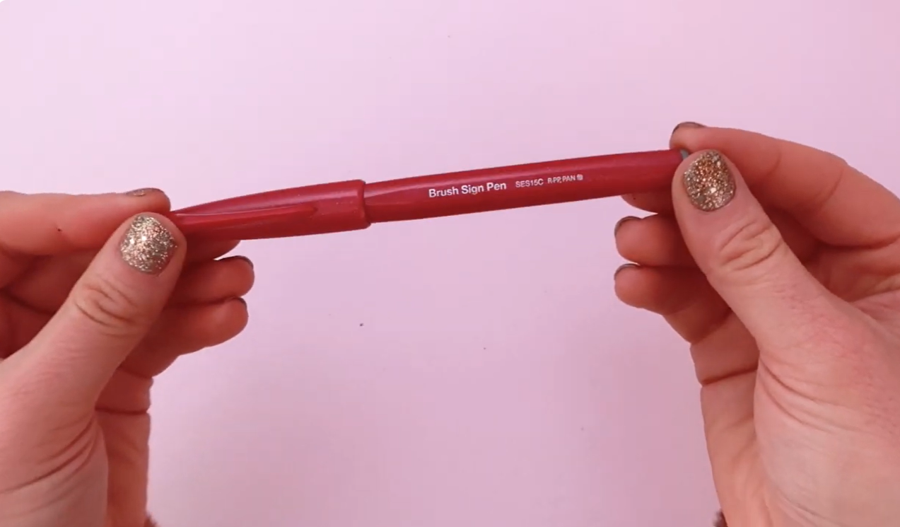 A Pentel Brush Sign Pen held up to the camera, showing the flexible brush nib tip used for modern calligraphy.