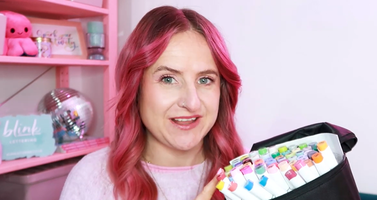 Milly, calligraphy tutor and founder of Blink Lettering, holding Ohuhu alcohol brush markers and smiling at the camera