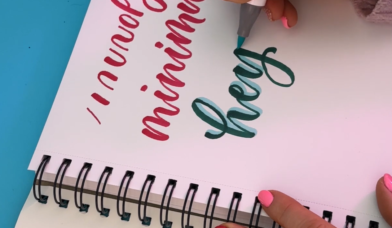 Calligraphy letters in pink with a turquoise green drop shadow added using Ohuhu alcohol markers, showing colour layering