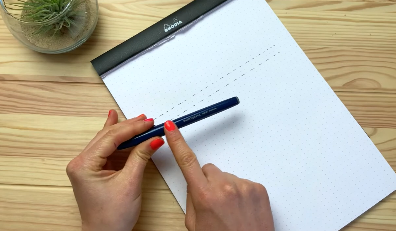Brush pen and dotted practice pad set up for learning basic calligraphy drills