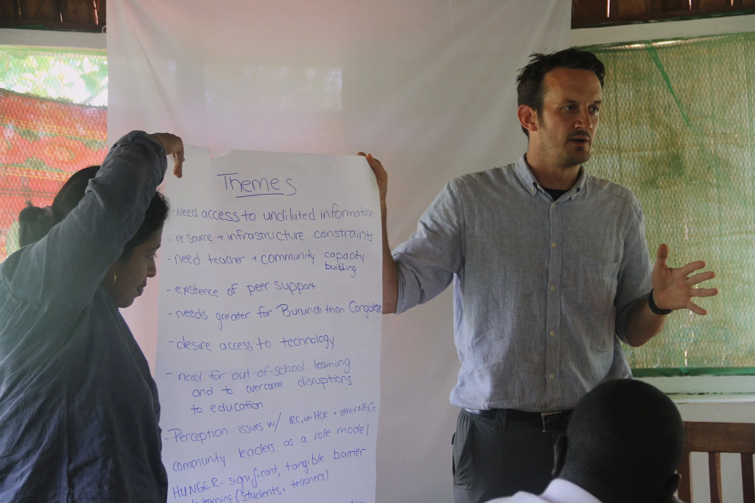 Man giving a presentation with a large poster listing themes, in a classroom or workshop setting.