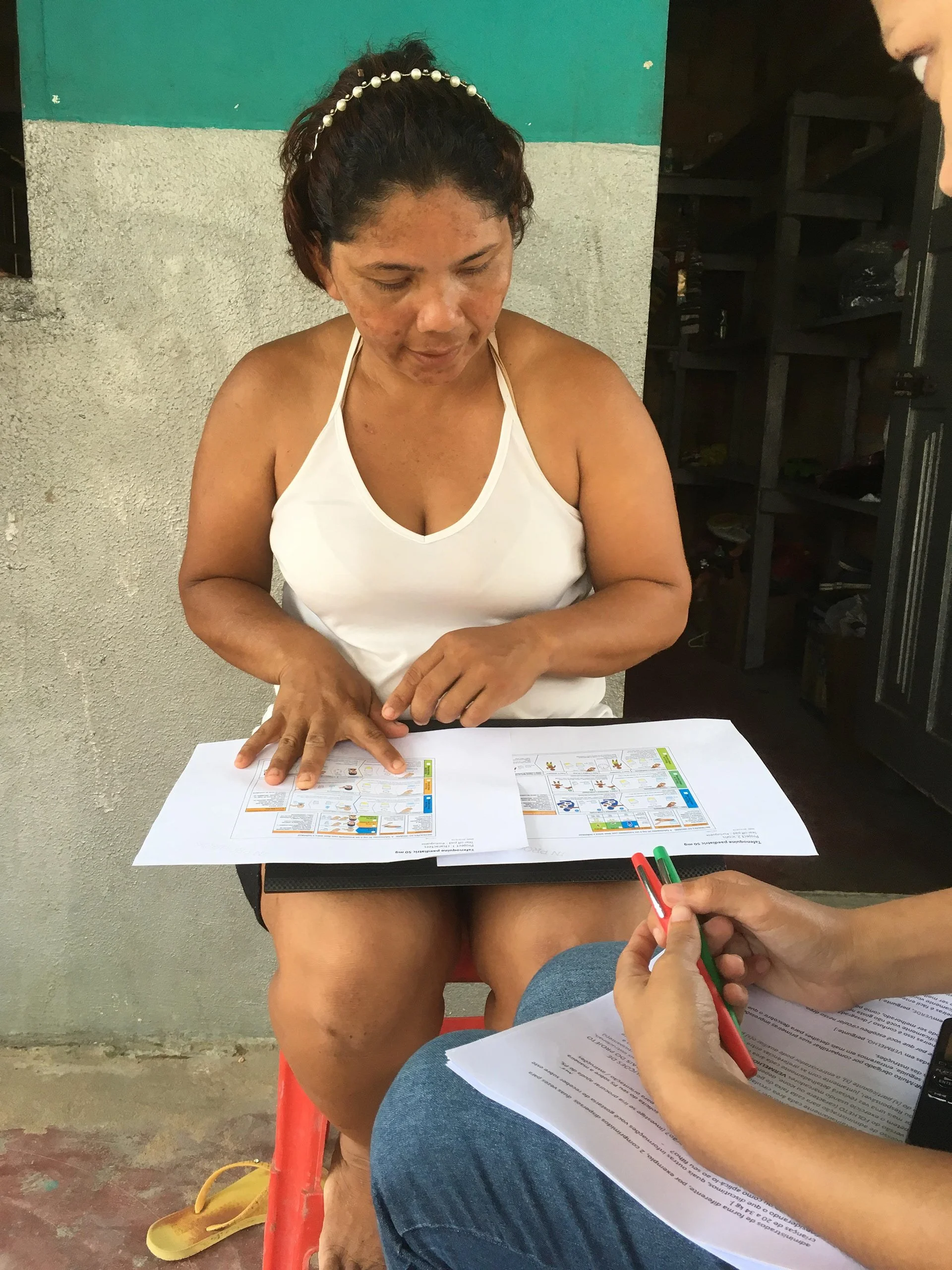 Woman in white tank top reviewing documents with another person holding pens.