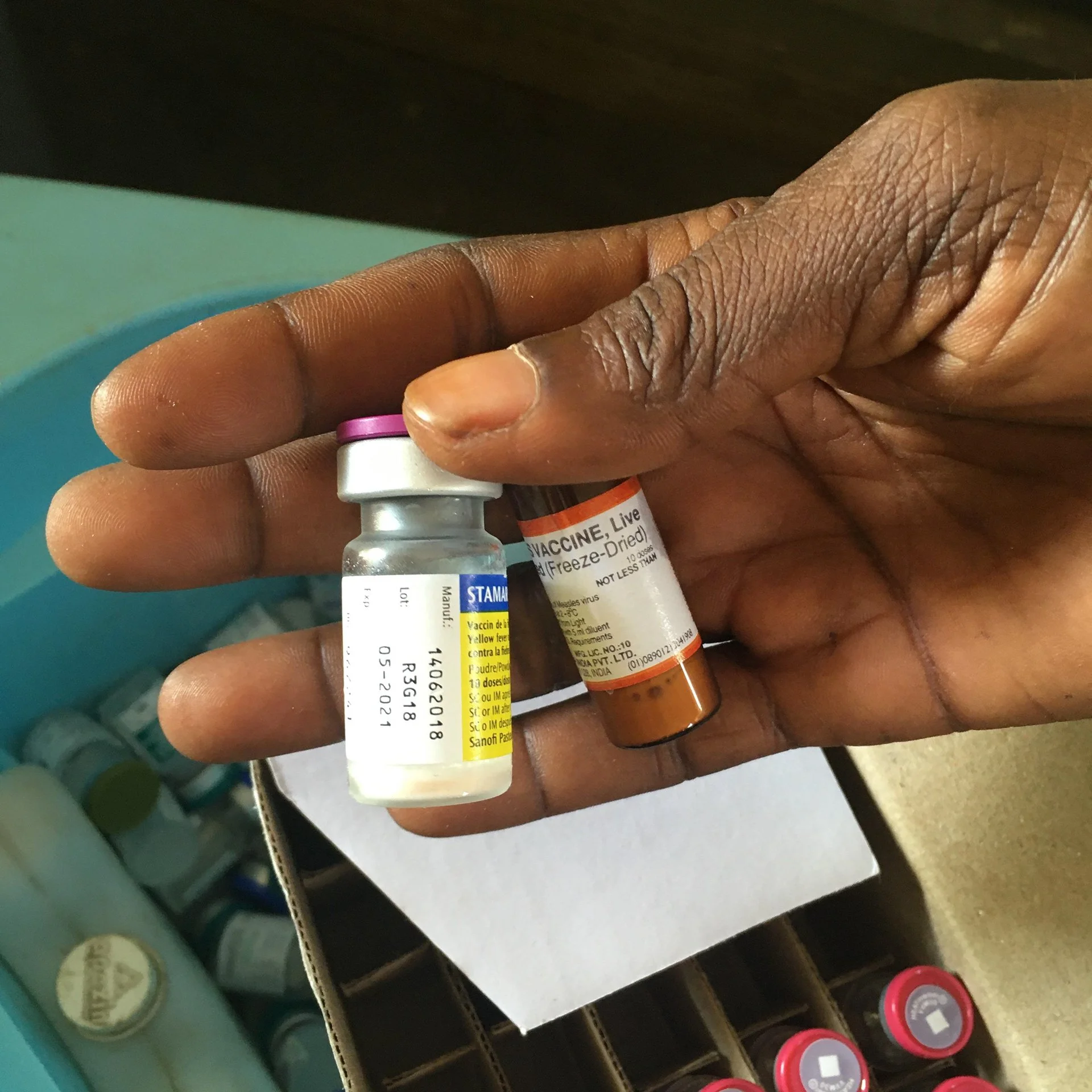 Close-up of a hand holding two vaccine vials with visible labels, surrounded by other medical supplies.
