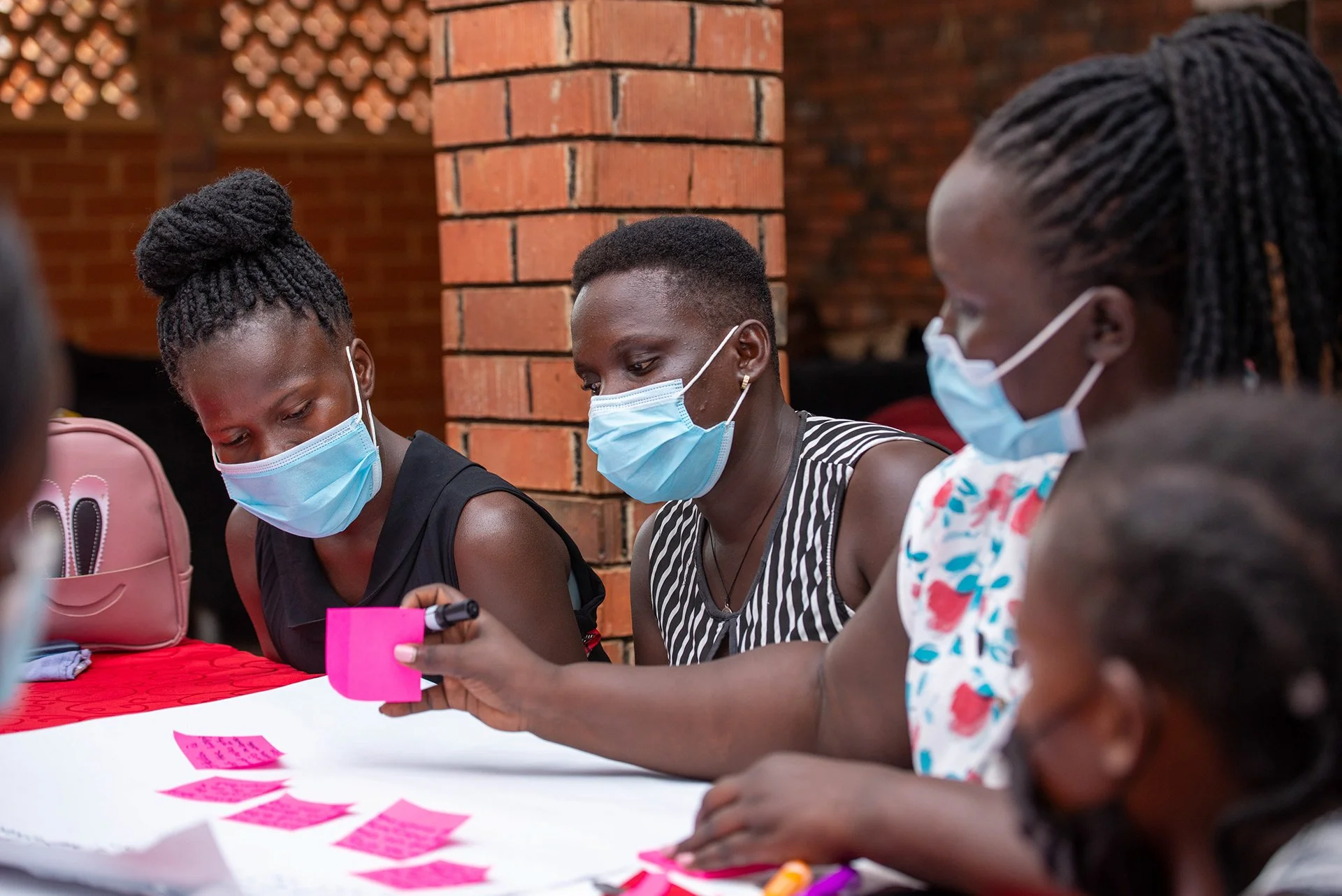 Group of people wearing masks collaborating with pink sticky notes at a table.