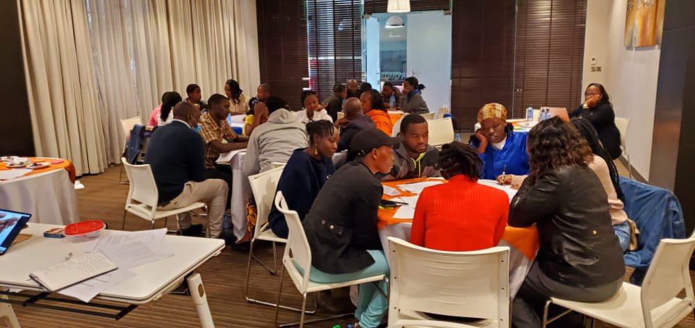 Group discussion in a workshop setting with people seated at tables, engaging in conversation and collaborating on tasks.