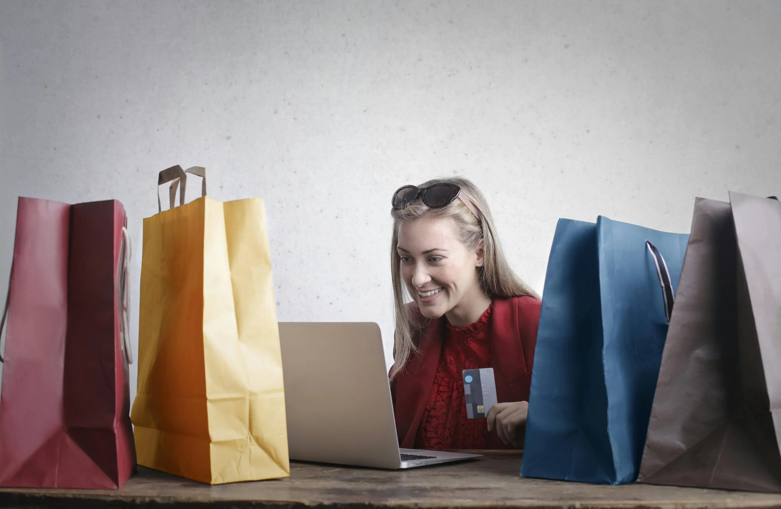 Woman shopping online with a credit card, surrounded by colorful shopping bags and using a laptop.