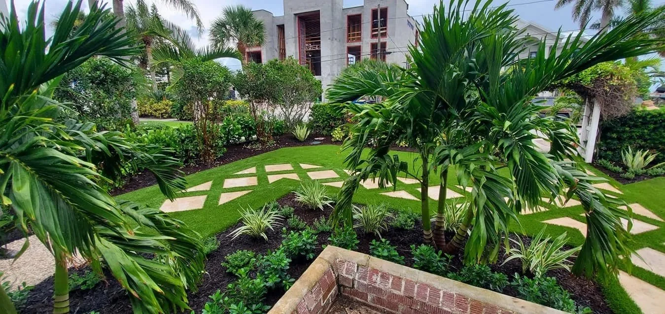 A landscaped garden with palm trees, green shrubs, grass, and a stone walkway.