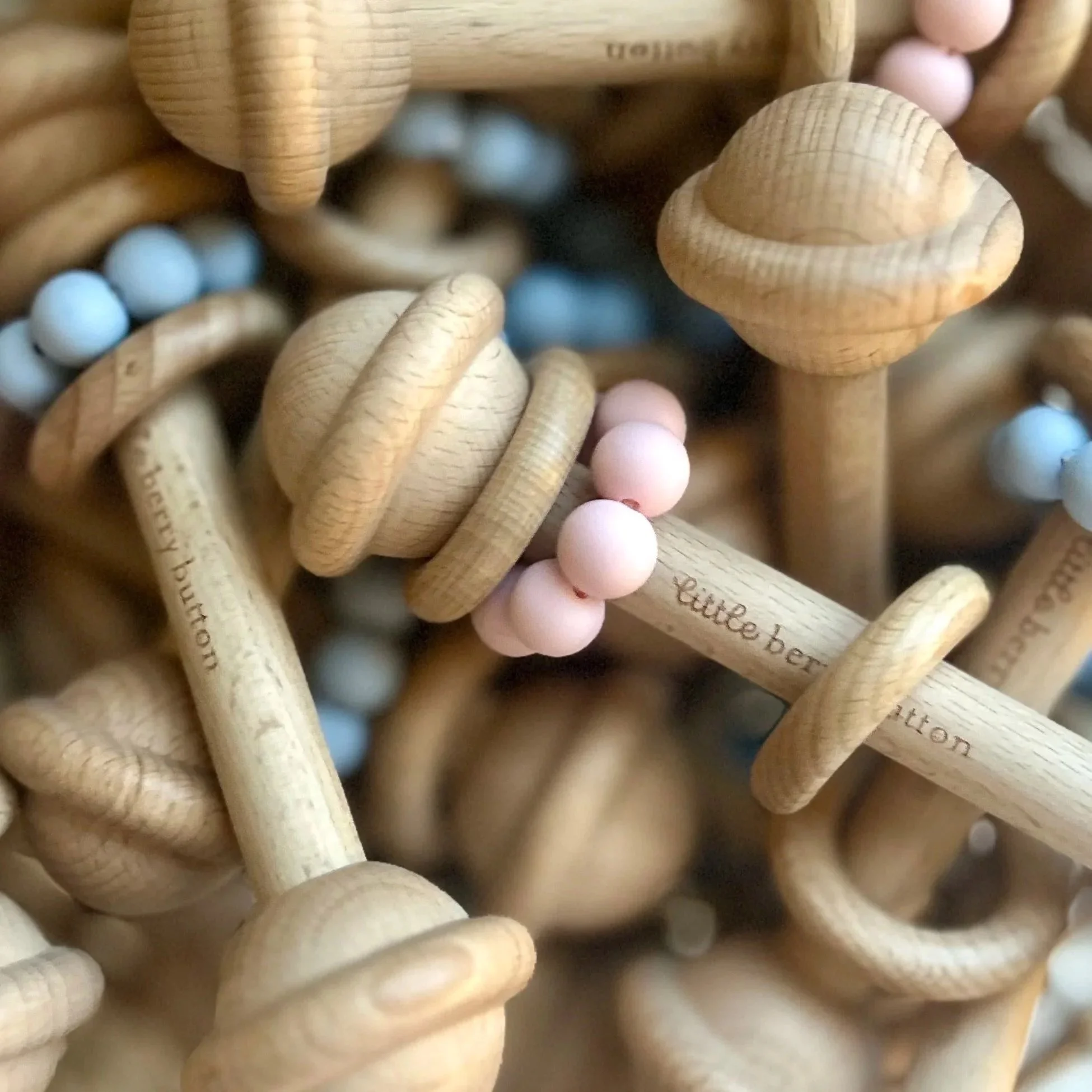 Wooden sensory teething rattles engraved with Little Berry Button Logo. Sensory teething rings are blue and pink and are all stacked on top of each other. Natural Beech wood.