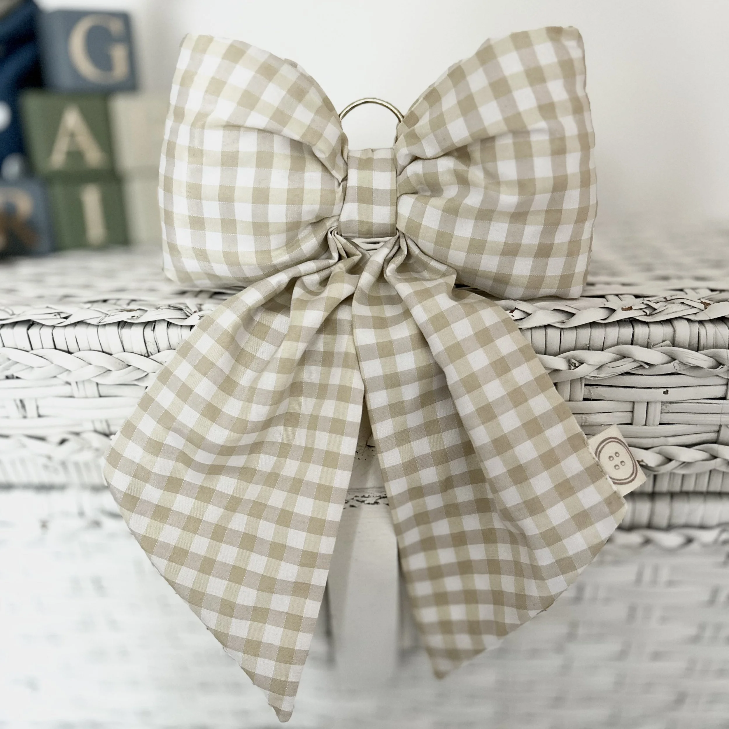 Cream Gingham polka dot fabric bow sitting on a white wicker style basket. Perfect for nursery decor