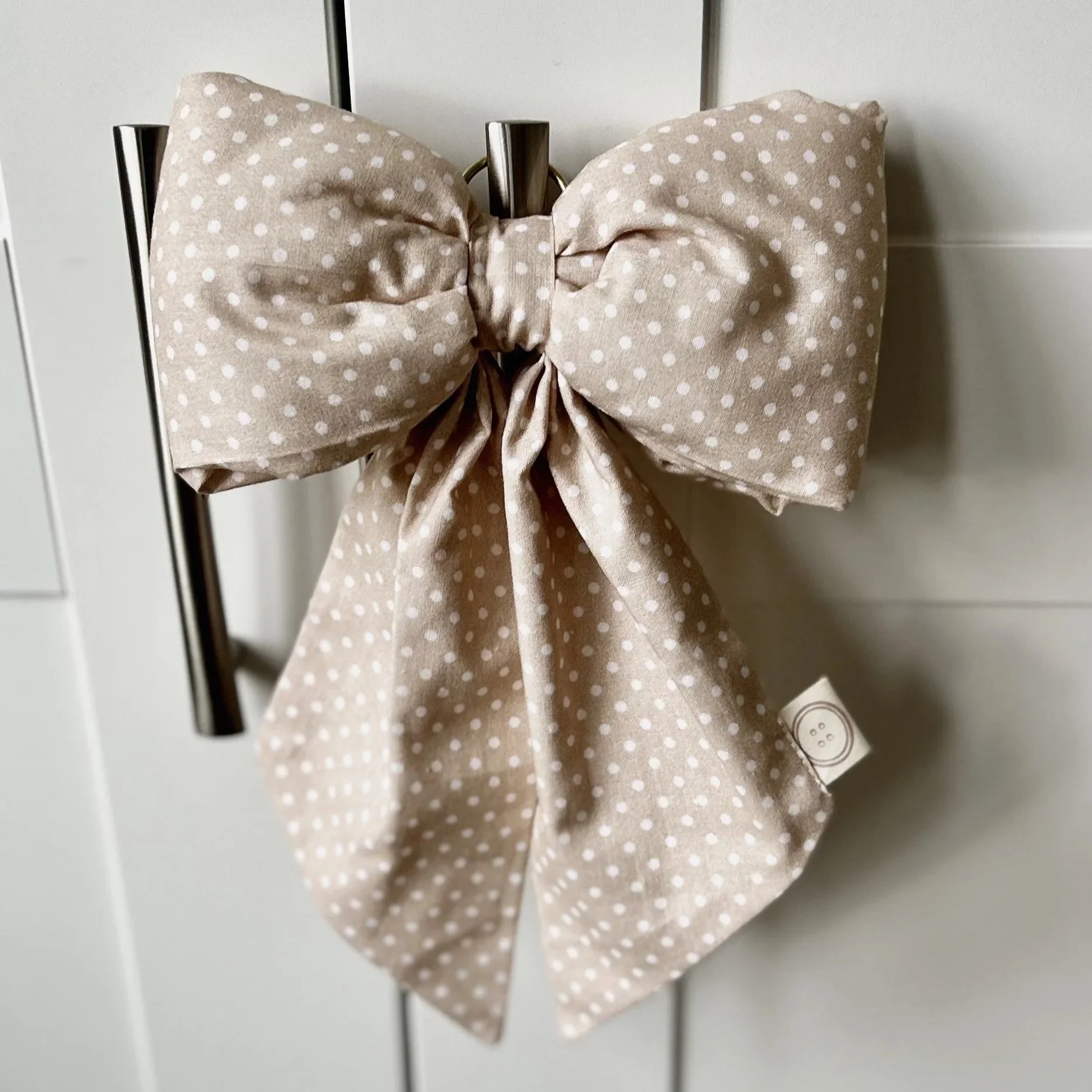 Salmon polka dot fabric bow hanging from a hook on a white background. Perfect for nursery decor