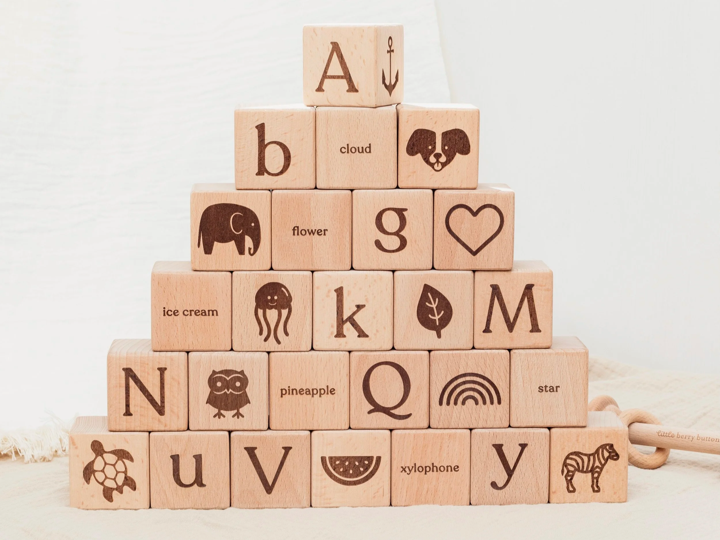 Wooden alphabet blocks stacked in a pyramid shape. Each block has 4 sides engraved with the capital letter the lower case letter, a picture of an item or animal starting with that particular letter and also the written word. Natural Beech Wood.