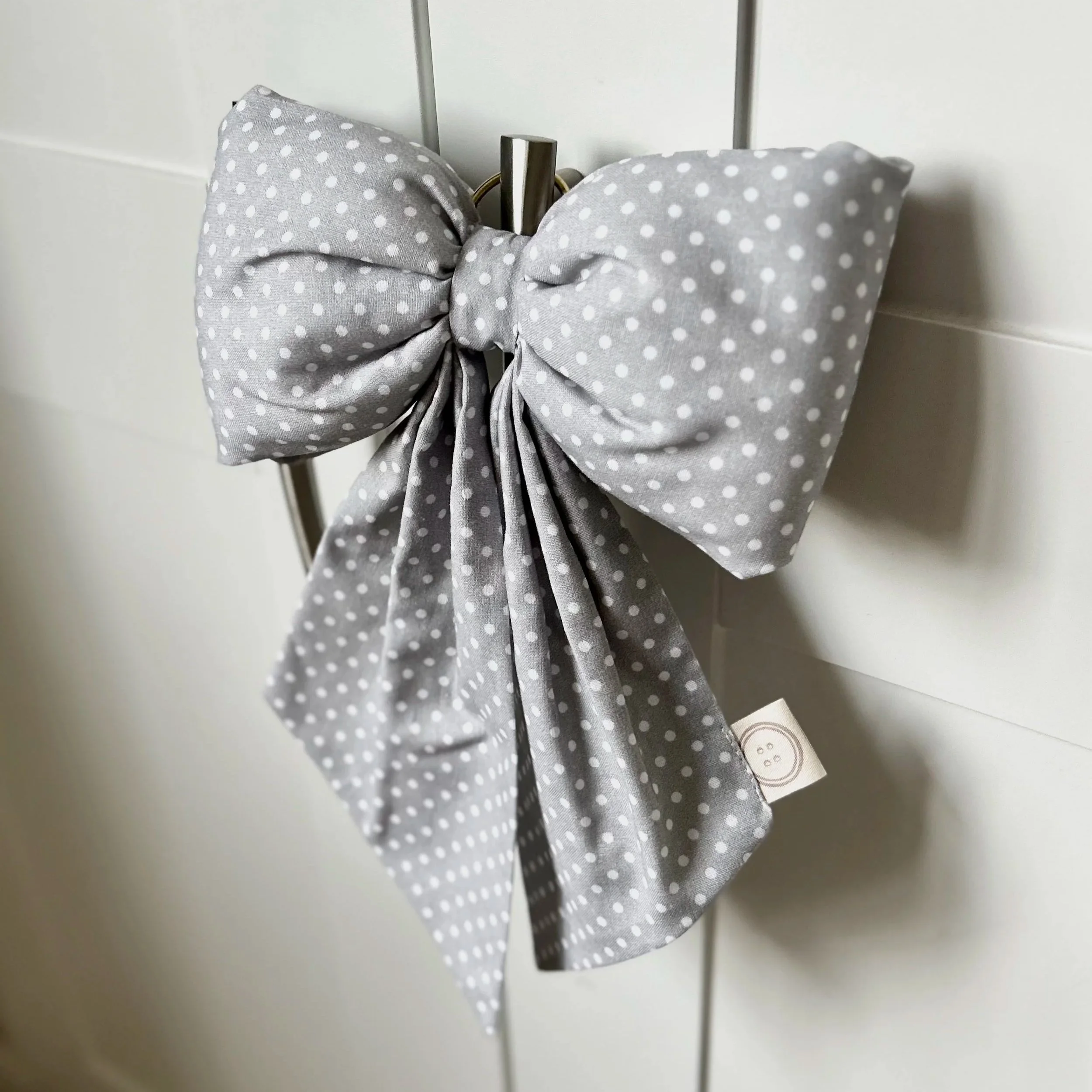 Blue/grey polka dot fabric bow hanging from a hook on a white background. Perfect for nursery decor