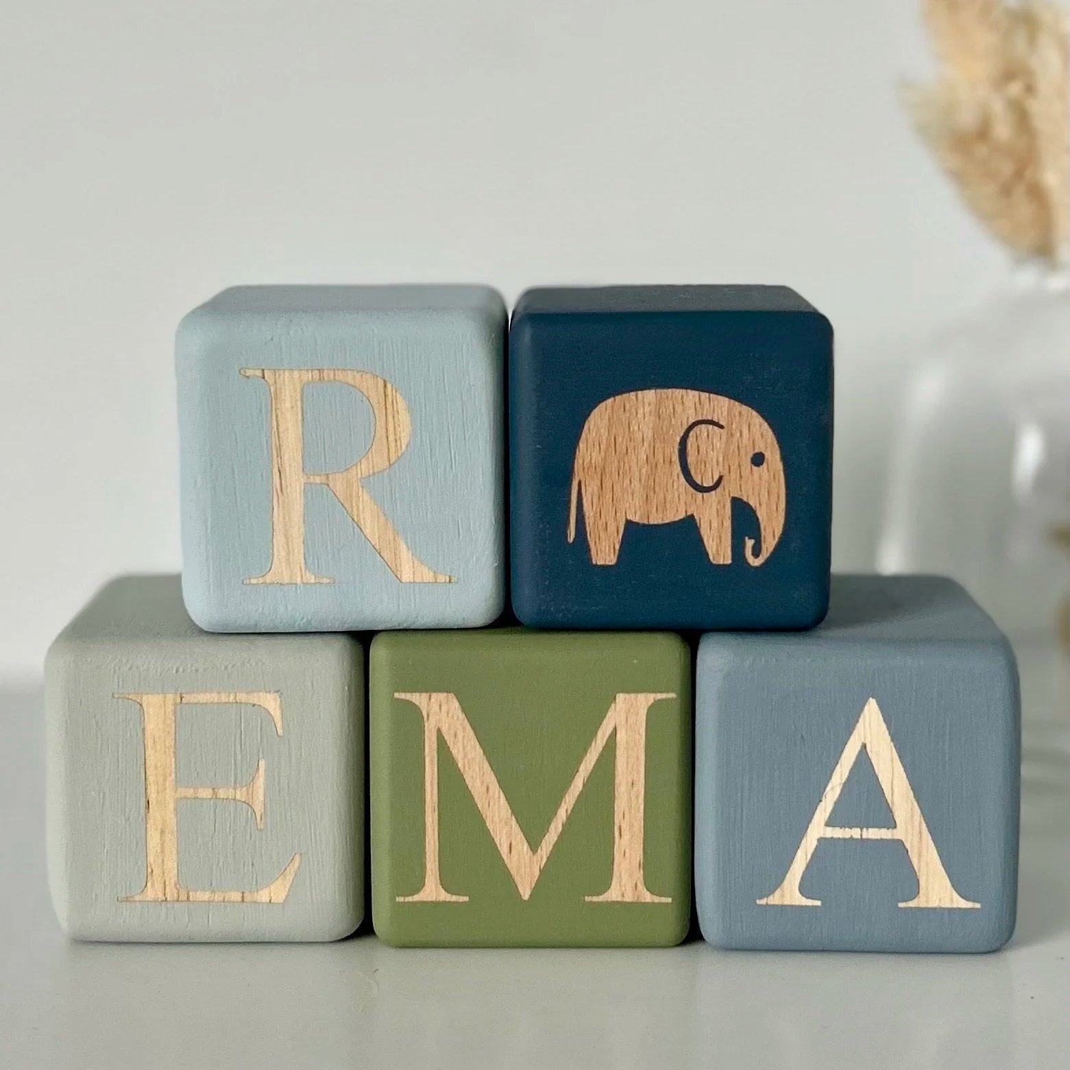 Personalised and hand painted name blocks in Classic Font that spell the name Reema in blue and green tones. They are stacked in two levels with R and E at the top and E, M and A on the bottom section.