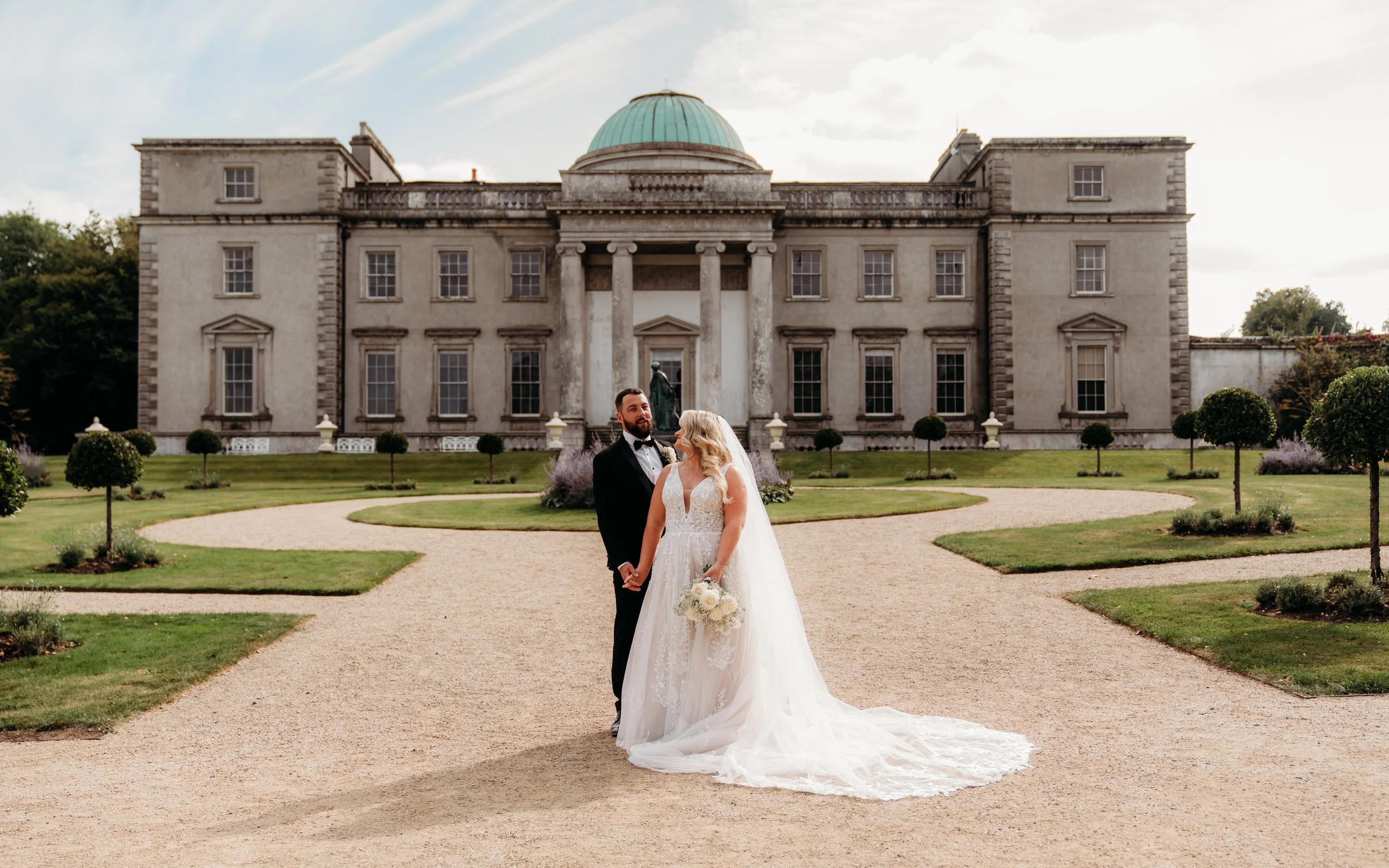 Bride and groom standing outside a grand estate in Ireland, classic documentary-style portrait.