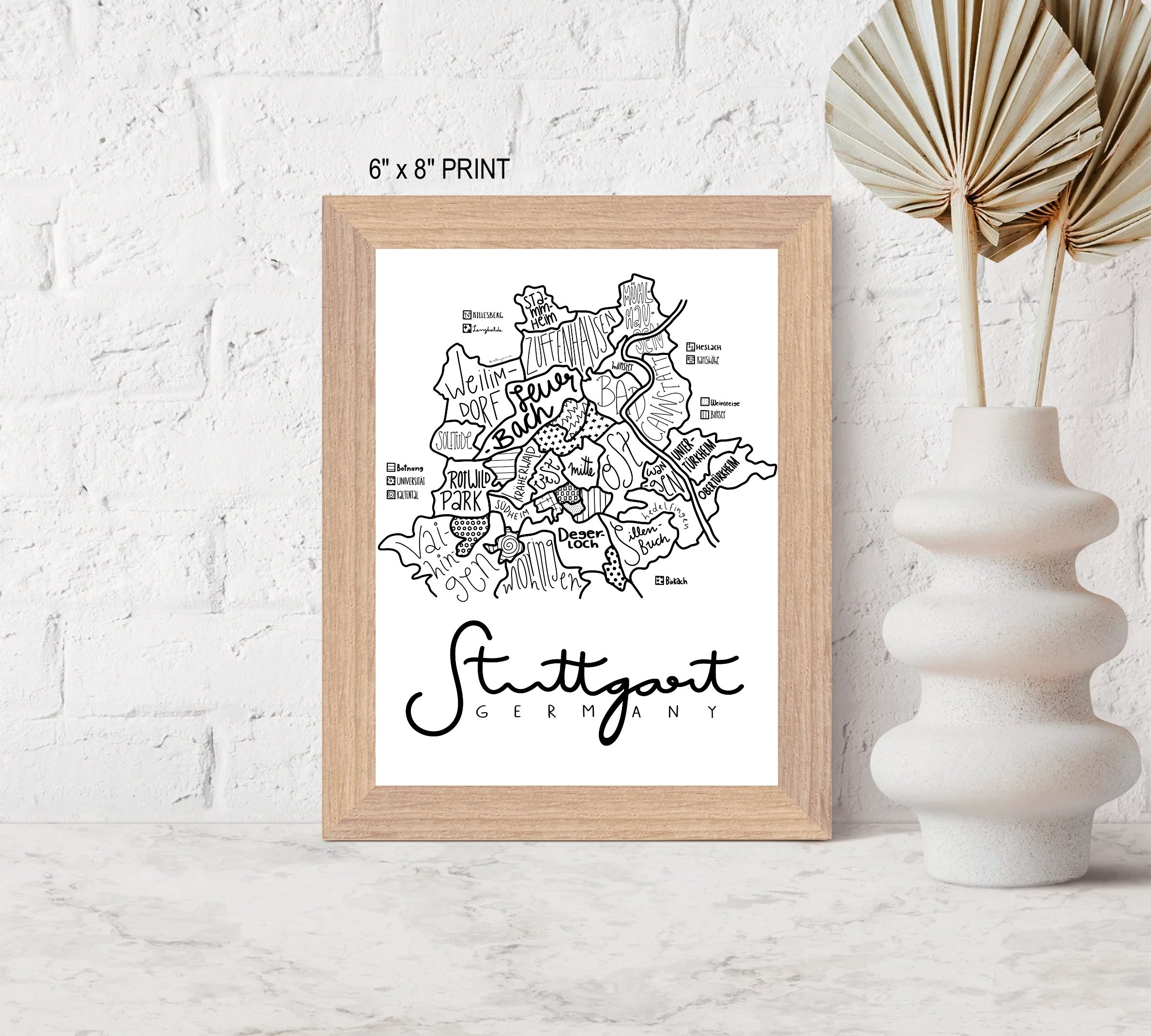 Small framed illustrated map of Stuttgart displayed on a table beside a decorative vase.