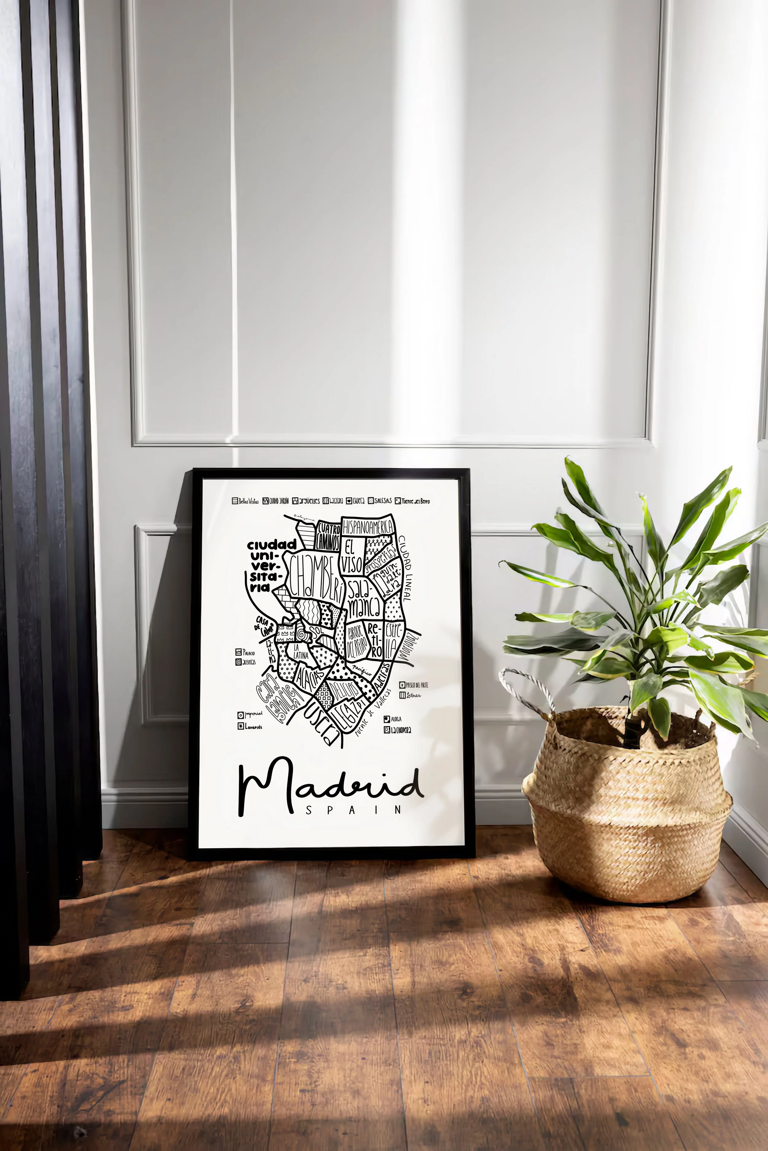 Black wood framed illustrated map of Madrid leaning against a wall in a modern apartment interior.