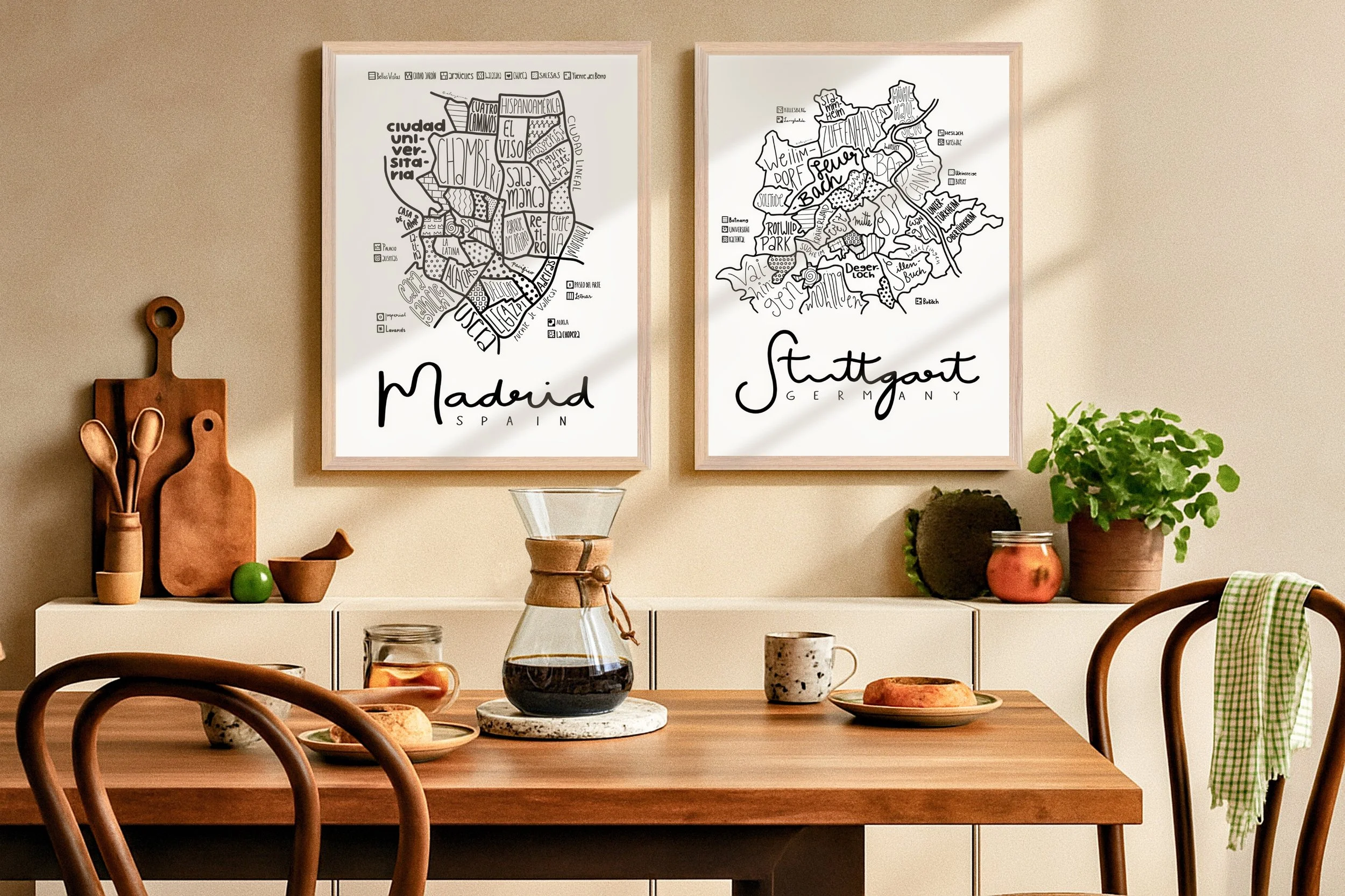 Illustrated map of Stuttgart in a natural wood frame displayed above a dining table, paired with another framed map.