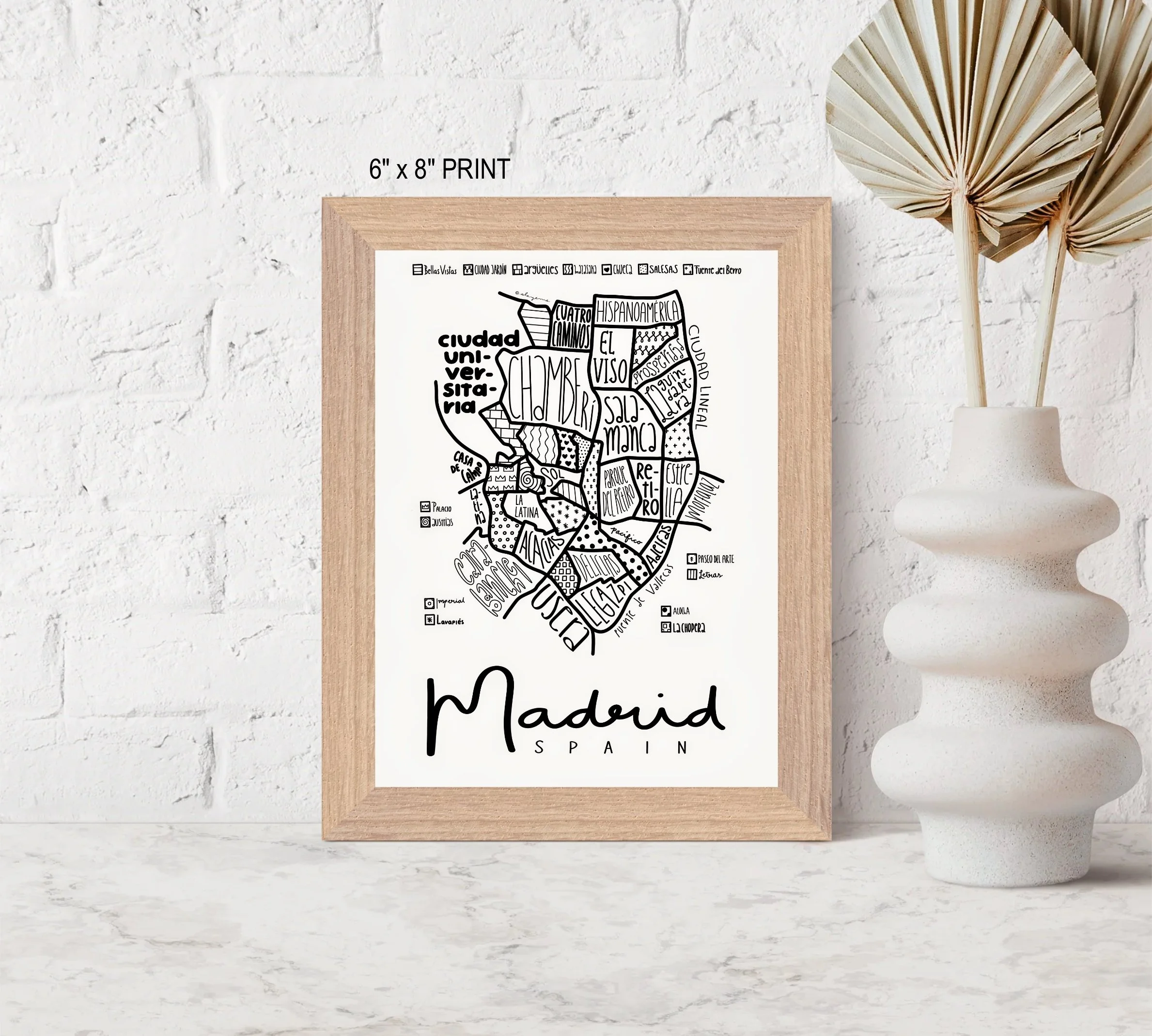 Small framed illustrated map of Madrid displayed on a table beside a decorative vase.