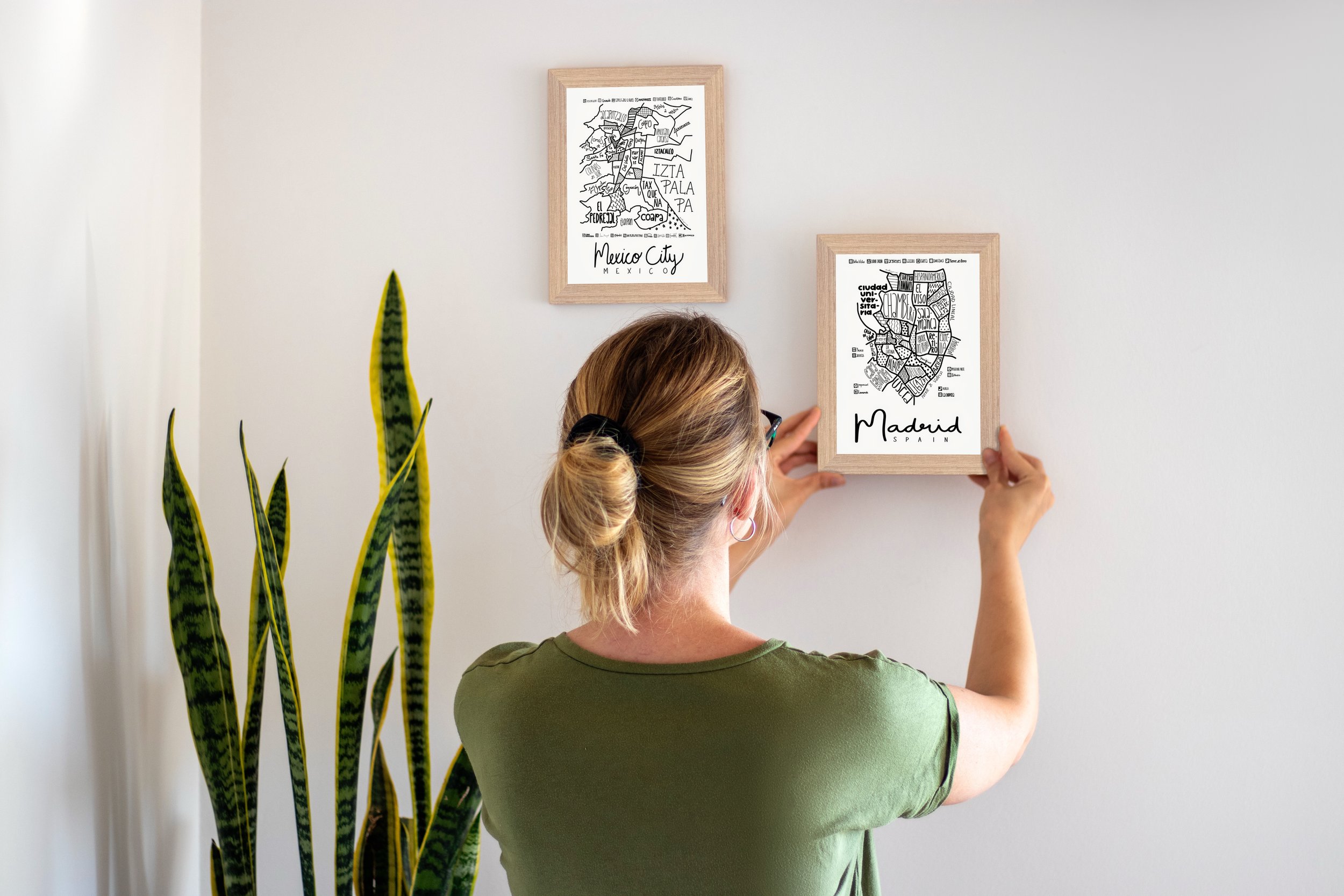 Two small framed illustrated maps being hung on a wall, with the Madrid map featured on the right.