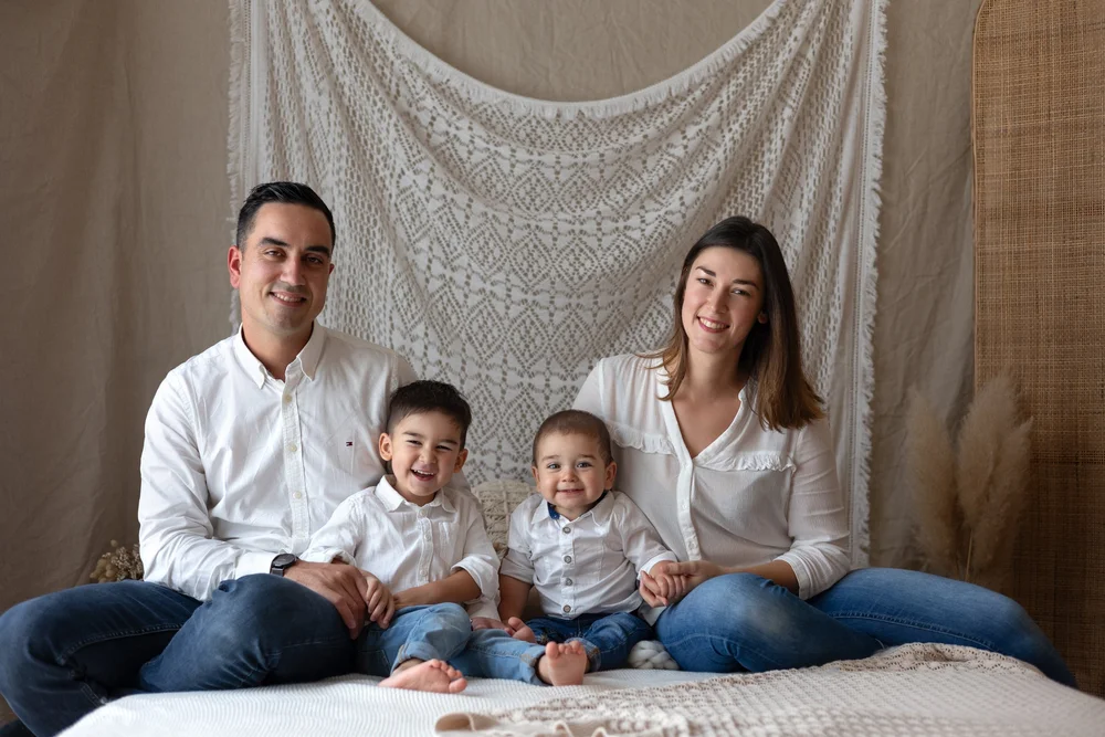 Famille de quatre assise sur un lit devant un paravent en rotin.