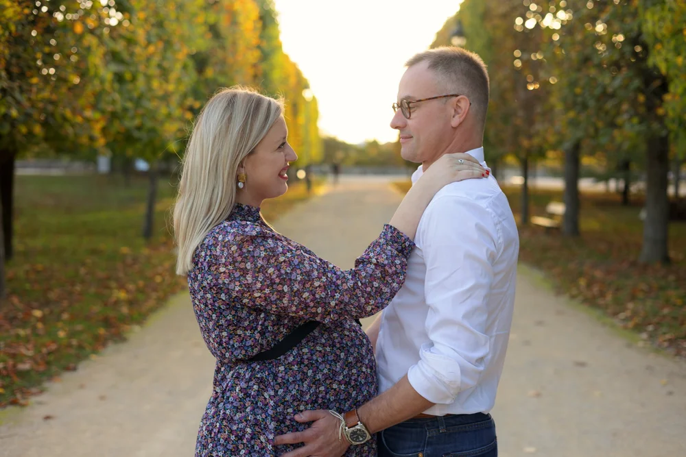 Couple dans une allée d’arbres en automne, la femme enceinte en robe fleurie.