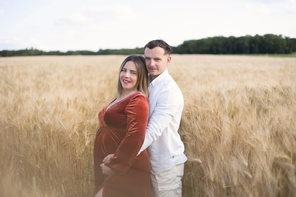 Couple dans un champ de blé, la femme enceinte en robe rouge.